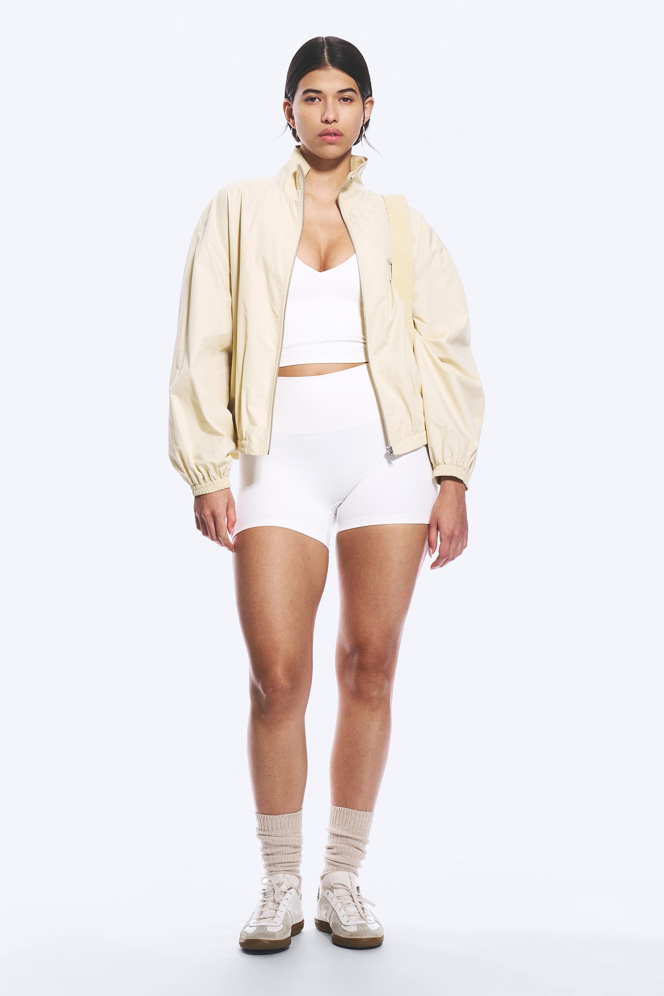 Größeres Bild ansehen: Weiße hoch taillierte Radler-Shorts mit breitem Bund, nahtlosen Außenseiten und umgeschlagenem Saum werden vom Model getragen. Diese Shorts in mittlerer Oberschenkellänge werden mit einem weißen Crop-Top und einer cremefarbenen Jacke kombiniert.