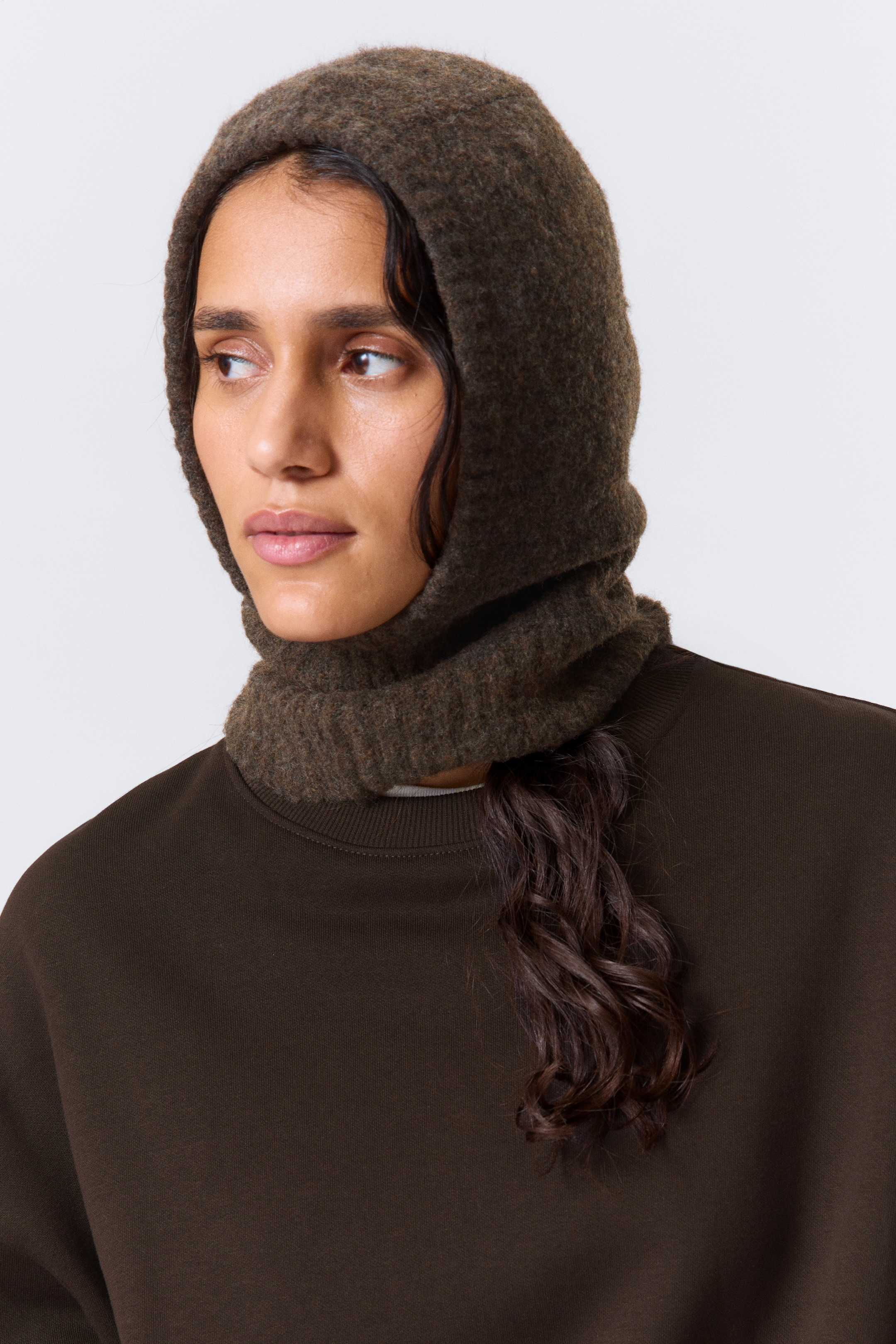 View larger image: A dark brown balaclava is covering the head and neck, featuring a felted texture on its hood and a ribbed knit on the neck portion. It is layering over a dark brown crewneck sweatshirt, which is displaying a ribbed collar.