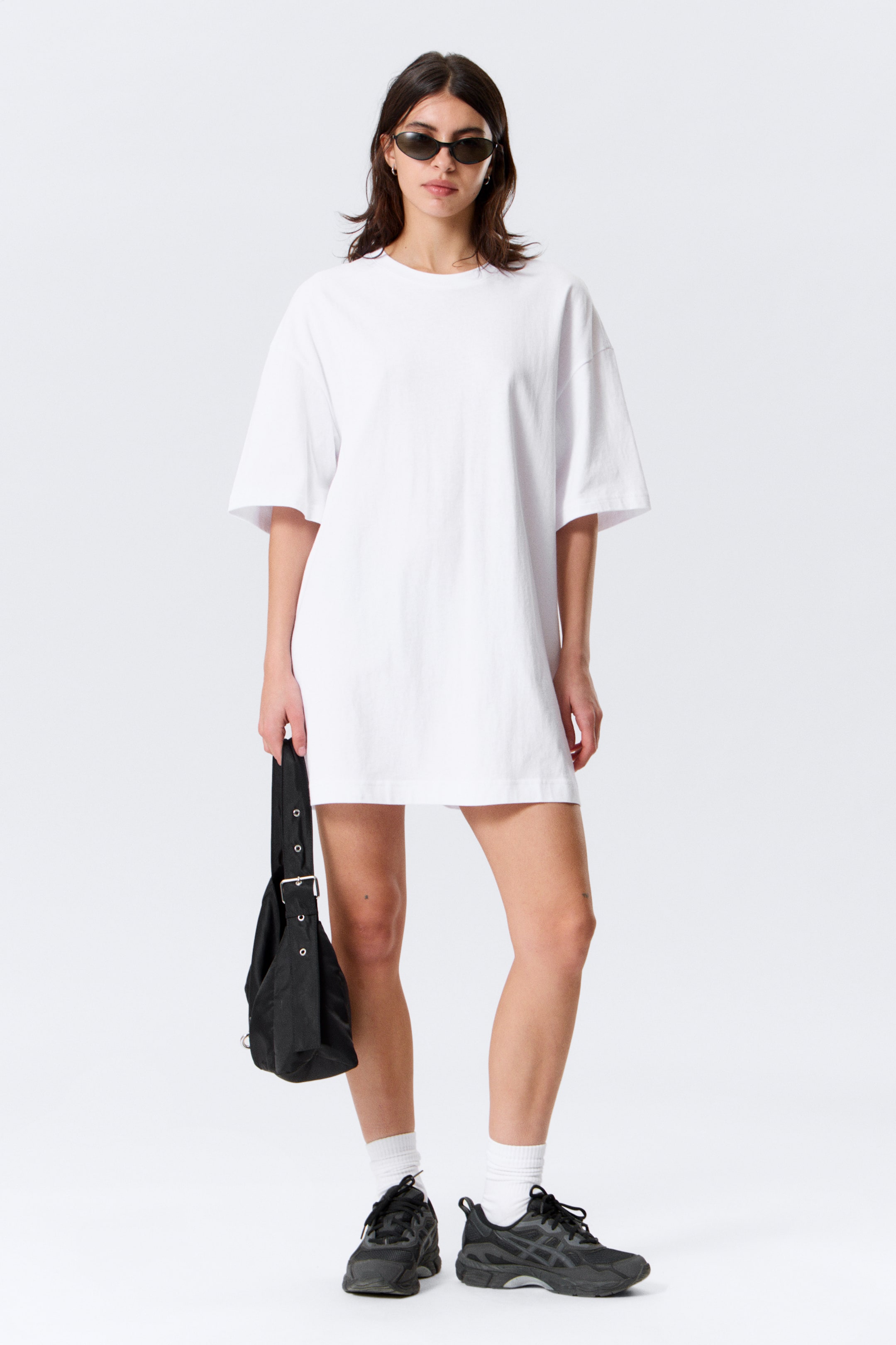 Grotere afbeelding bekijken: Een witte oversized t-shirt jurk met een ronde hals, korte wijde mouwen en een ontspannen pasvorm, waarbij de zoomlijn boven de knie valt.