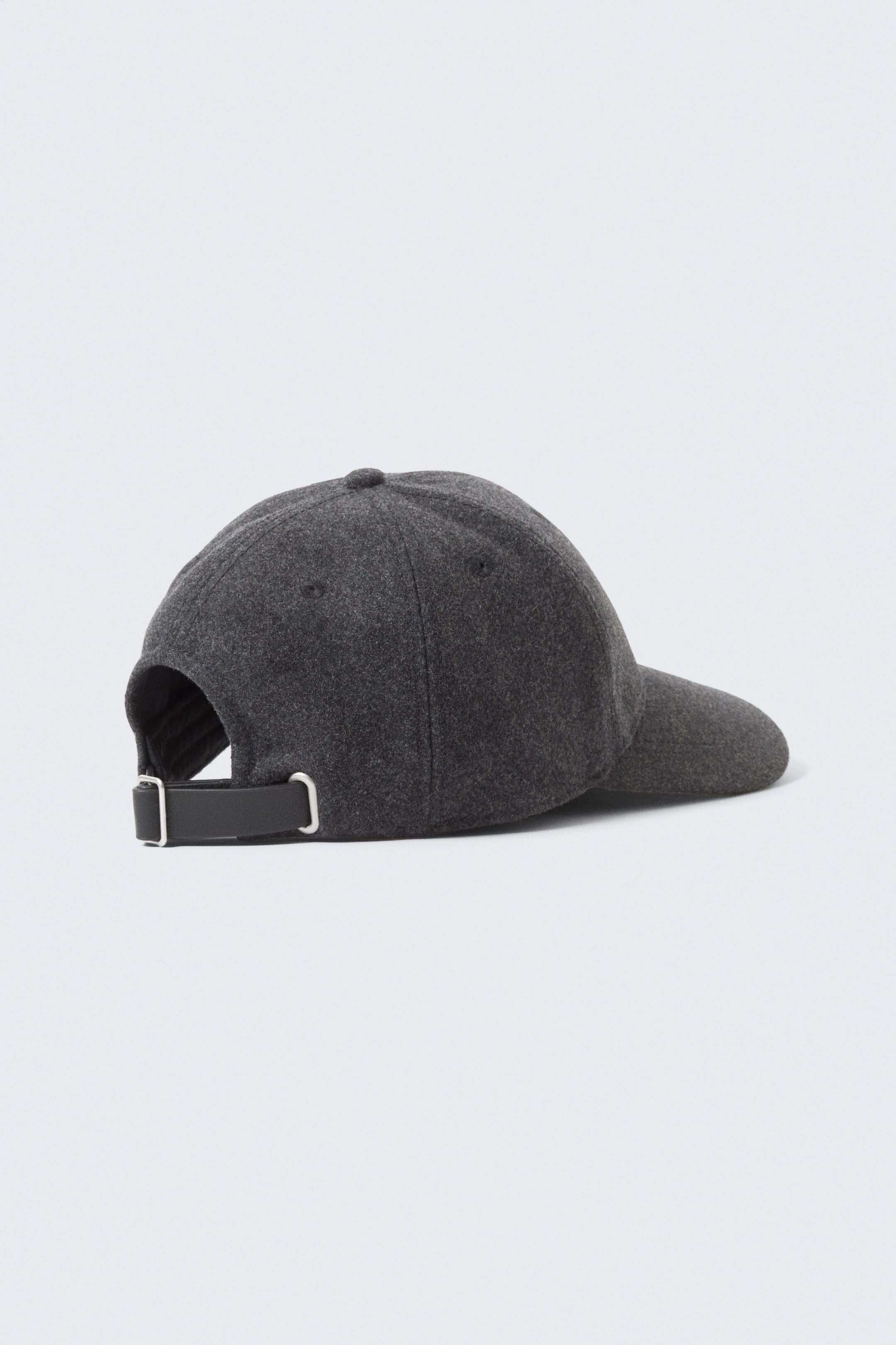 Ver imagen más grande: Se muestra una gorra de béisbol de color gris oscuro vista desde atrás, confeccionada con un material estructurado de mezcla de lana. Presenta una visera precurvada, pequeños ojales de ventilación en el panel lateral y una correa ajustable de color negro con herrajes metálicos plateados en la parte trasera.