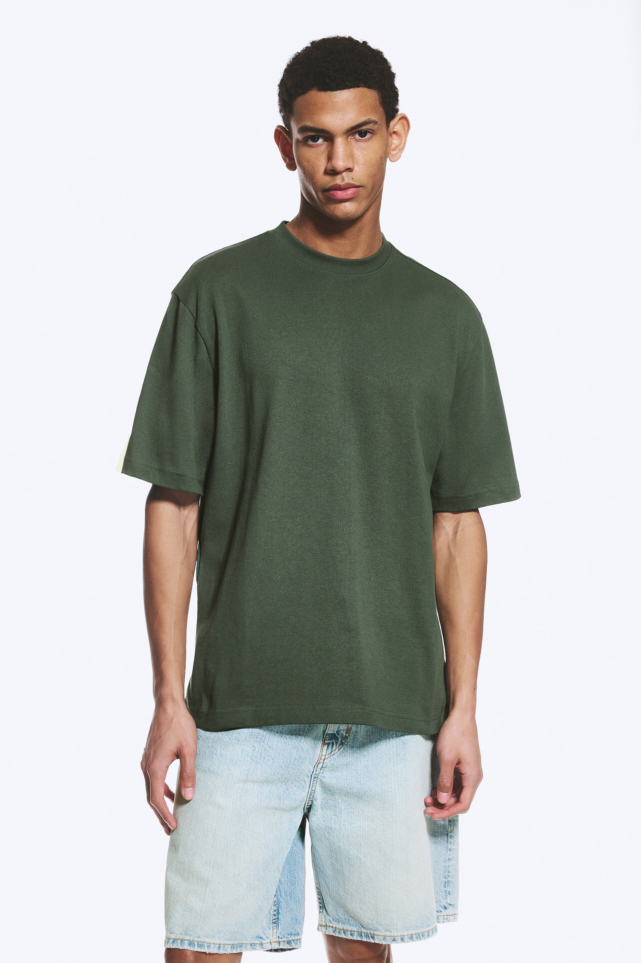 Ver imagem maior: Uma t-shirt verde escura está a ser apresentada, com decote redondo e mangas curtas. Apresenta um corte descontraído e um tecido subtilmente texturizado.