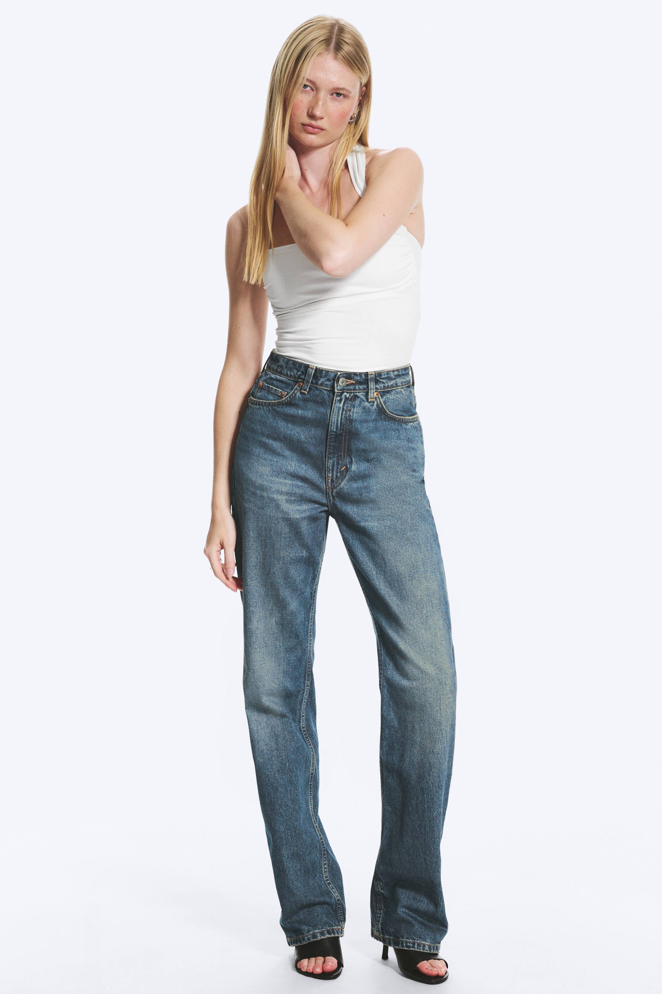 Vis større bilde: En hvit, asymmetrisk, ettersittende singlet med én skulder er stukket inn i høytlivs jeans i en medium blå vask, som har en avslappet rett passform.