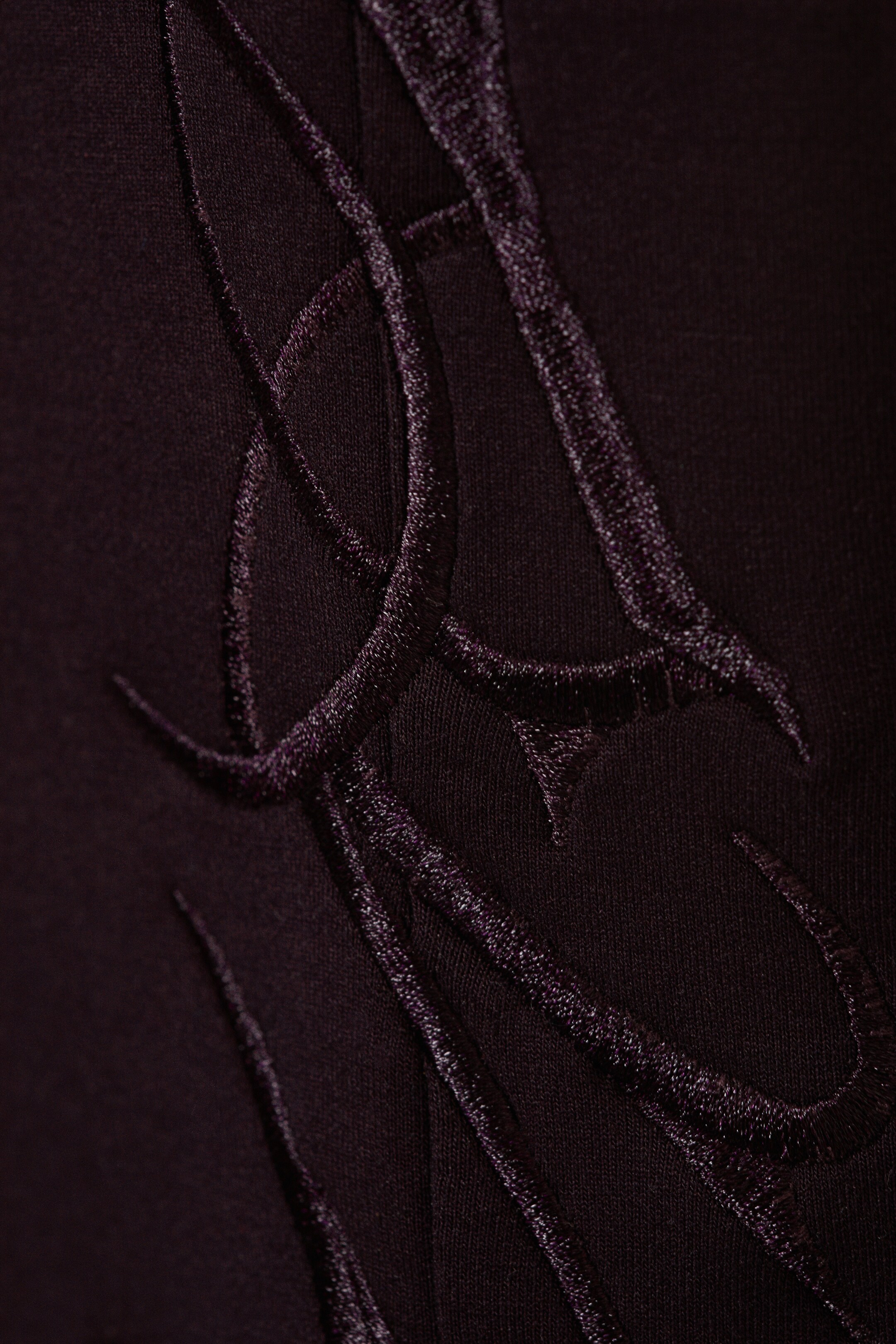 Agrandir l'image: Un textile sombre présente une broderie complexe et scintillante en violet foncé. La broderie en relief forme des motifs élaborés et tourbillonnants à la surface.
