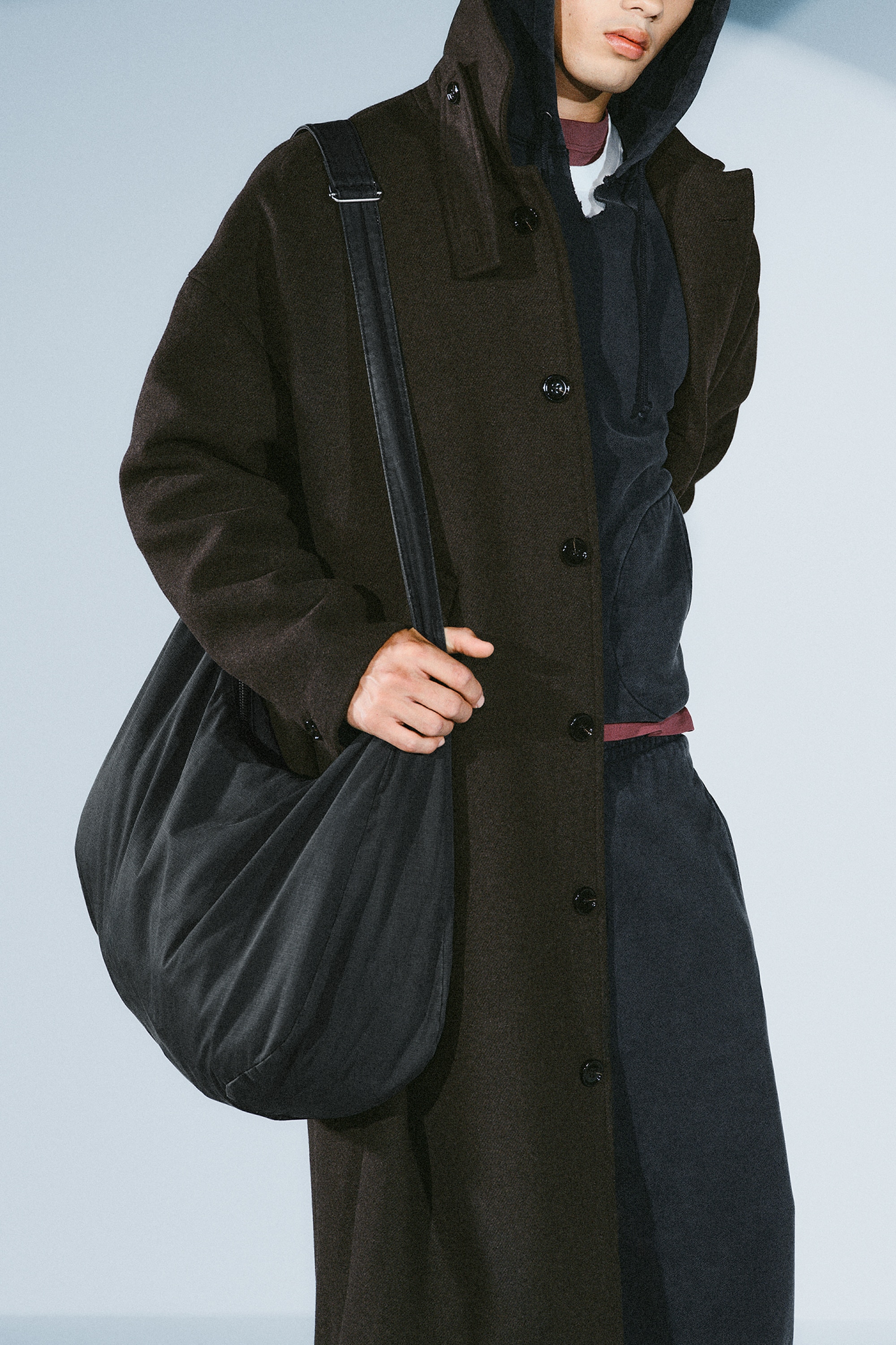 Eine dunkelgraue Stoff-Hobo-Tasche zeichnet sich durch eine weiche, halbmondförmige Silhouette und einen einzelnen verstellbaren Riemen mit silberfarbenem Versteller aus. Ein silberfarbener Reissverschluss verläuft entlang der oberen Öffnung.