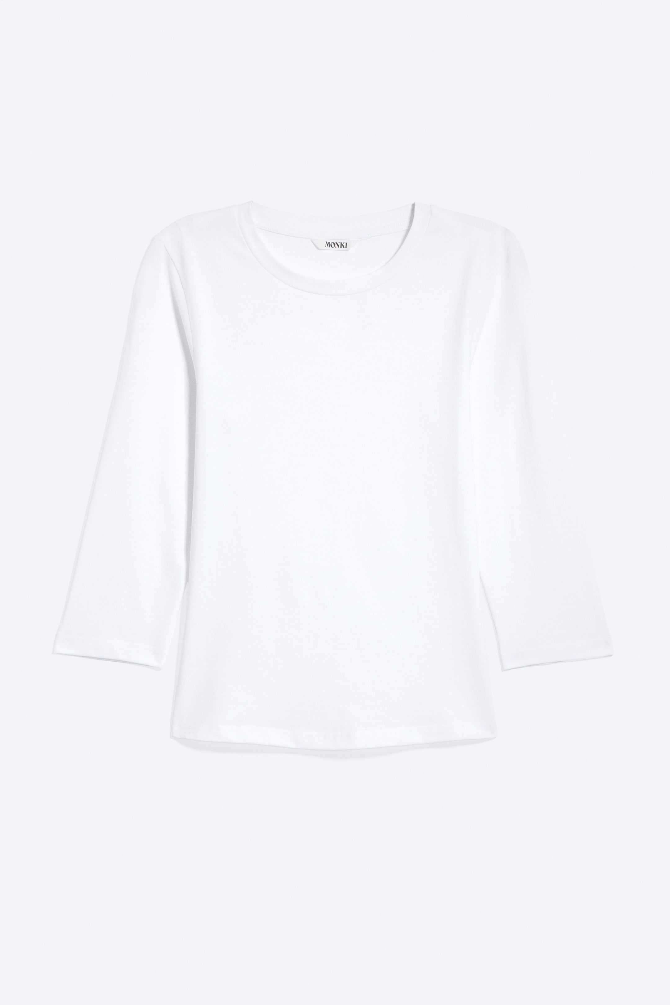 Se større billede: En hvid langærmet top præsenteres forfra, med en rund halsudskæring og 3/4-lange ærmer. Et "MONKI" mærkat er synligt bag på halsen.