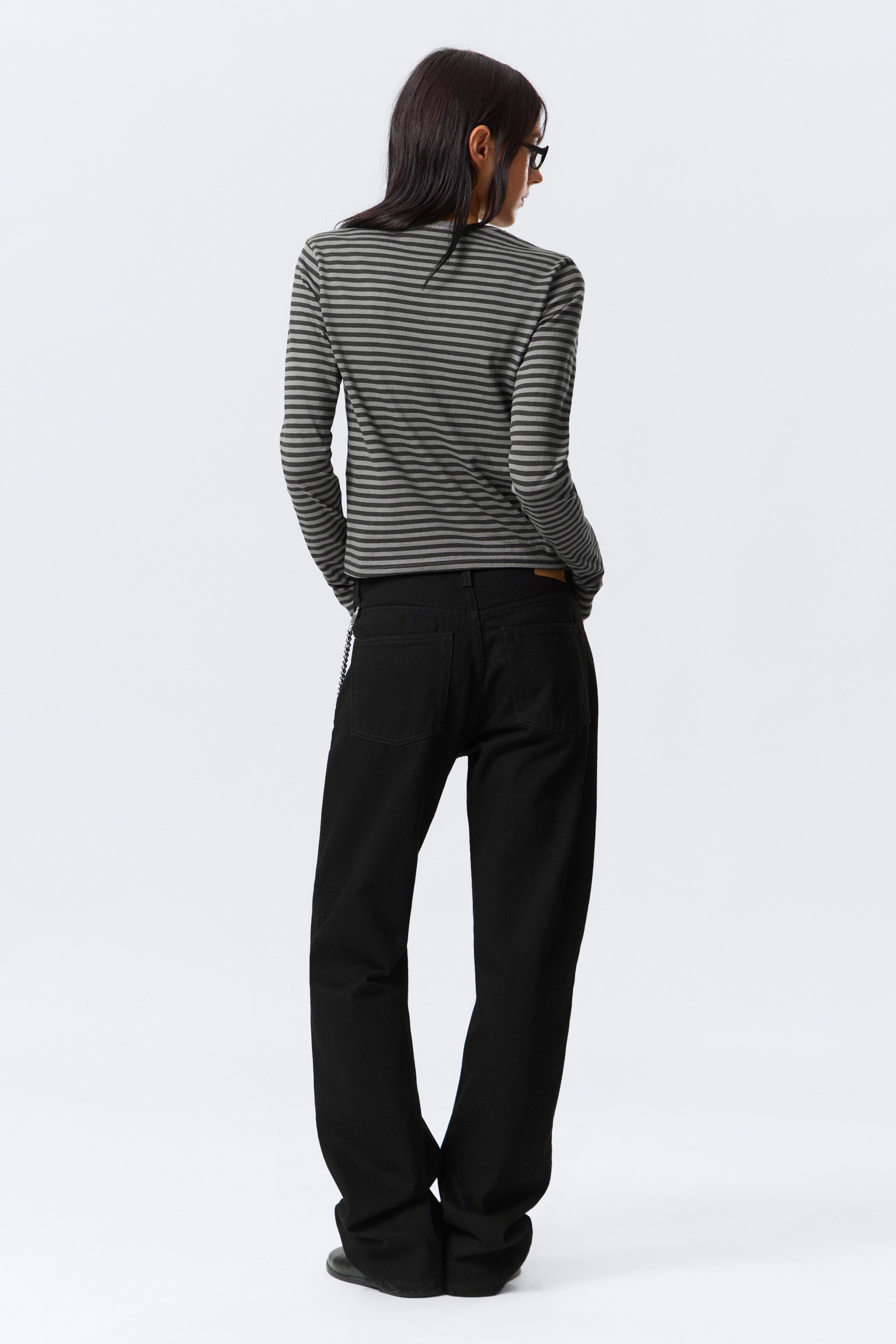 View larger image: A long-sleeve top featuring alternating dark gray and light gray horizontal stripes is being presented from the back, paired with black straight-leg jeans that are featuring back pockets and a small waistband tag.