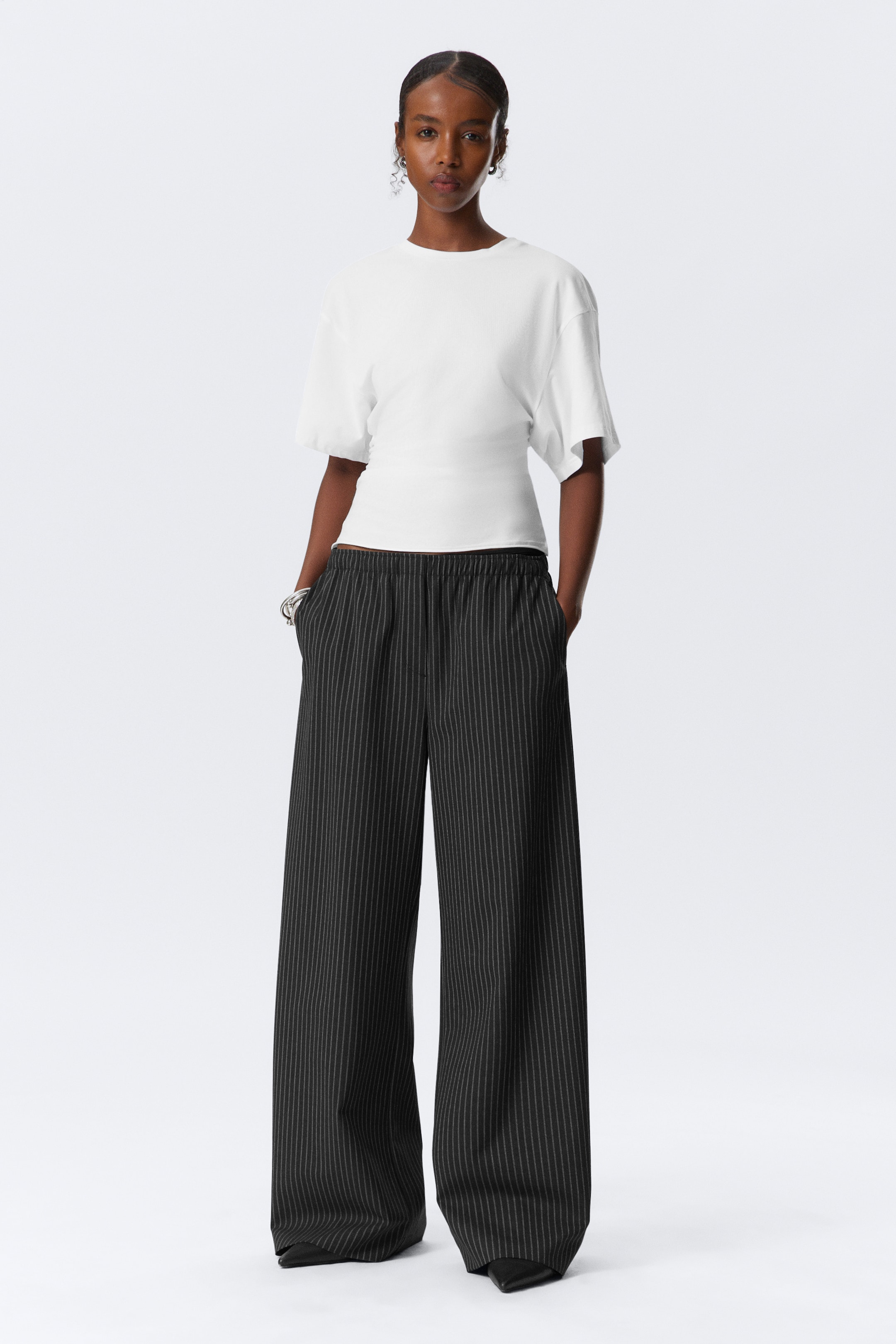 Agrandir l'image: Un haut blanc à col rond avec des manches courtes et amples et une taille cintrée est présenté de face. Il est associé à un pantalon noir à jambes larges avec de fines rayures blanches et une taille élastiquée.