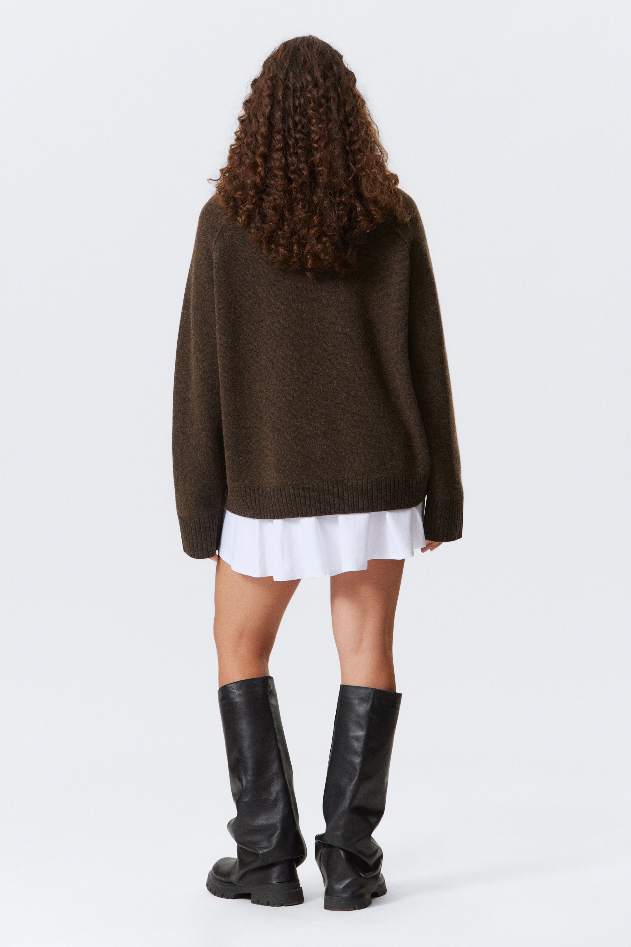 Agrandir l'image: Un pull en maille surdimensionné de couleur brun foncé est présenté de dos, avec une coupe décontractée, des manches longues et un ourlet côtelé. Une chemise blanche est superposée en dessous, avec son ourlet plissé visible sous le pull.