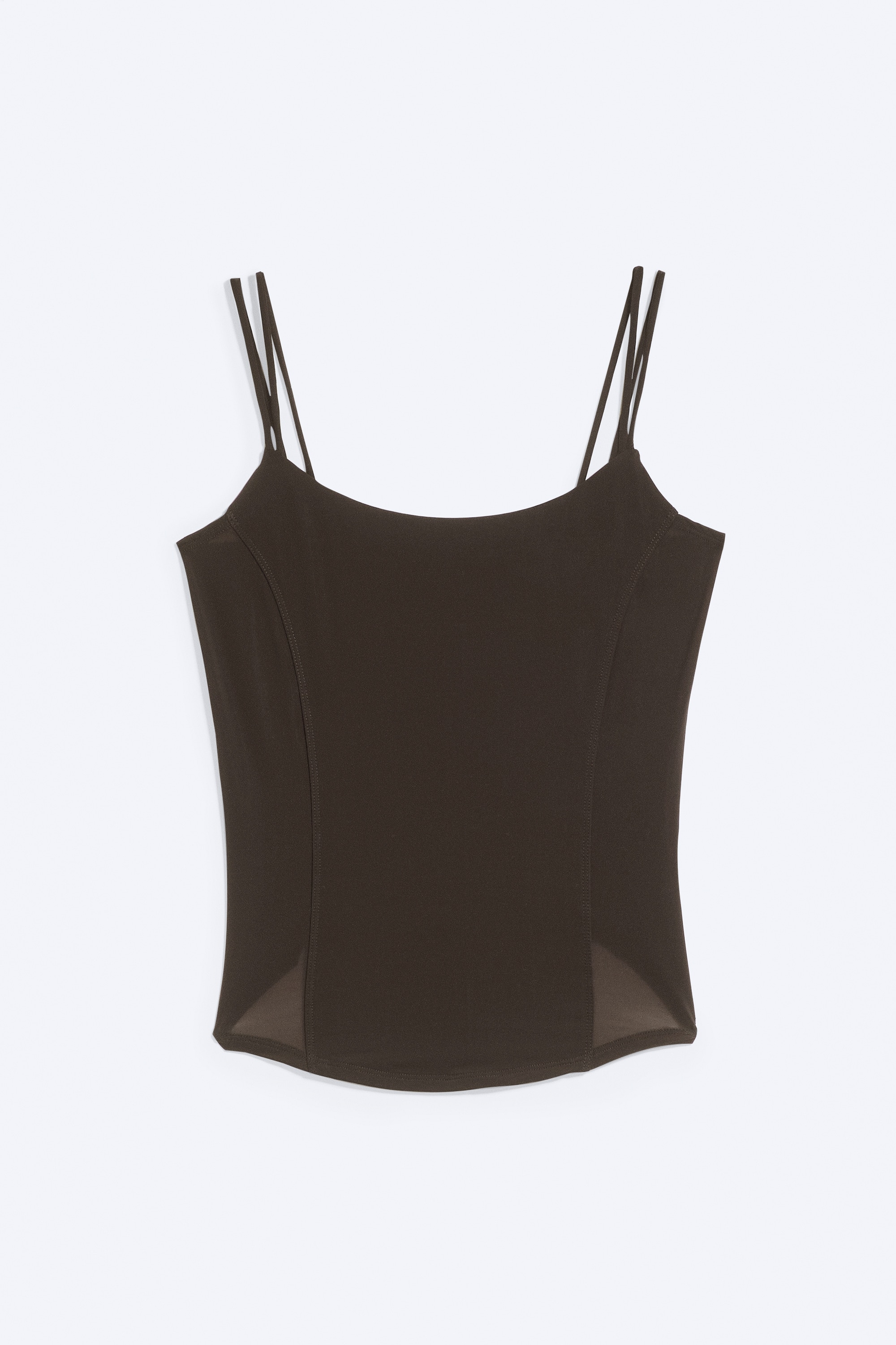 En mÃ¸rkebrun corsetop med slim fit bÃ¦res af modellen og har en rund halsudskÃ¦ring, tynde dobbelte skulderstropper og buede panelsÃ¸mme langs kroppen. Toppen er designet med en buet kant og er stylet med olivengrÃ¸nne bukser.