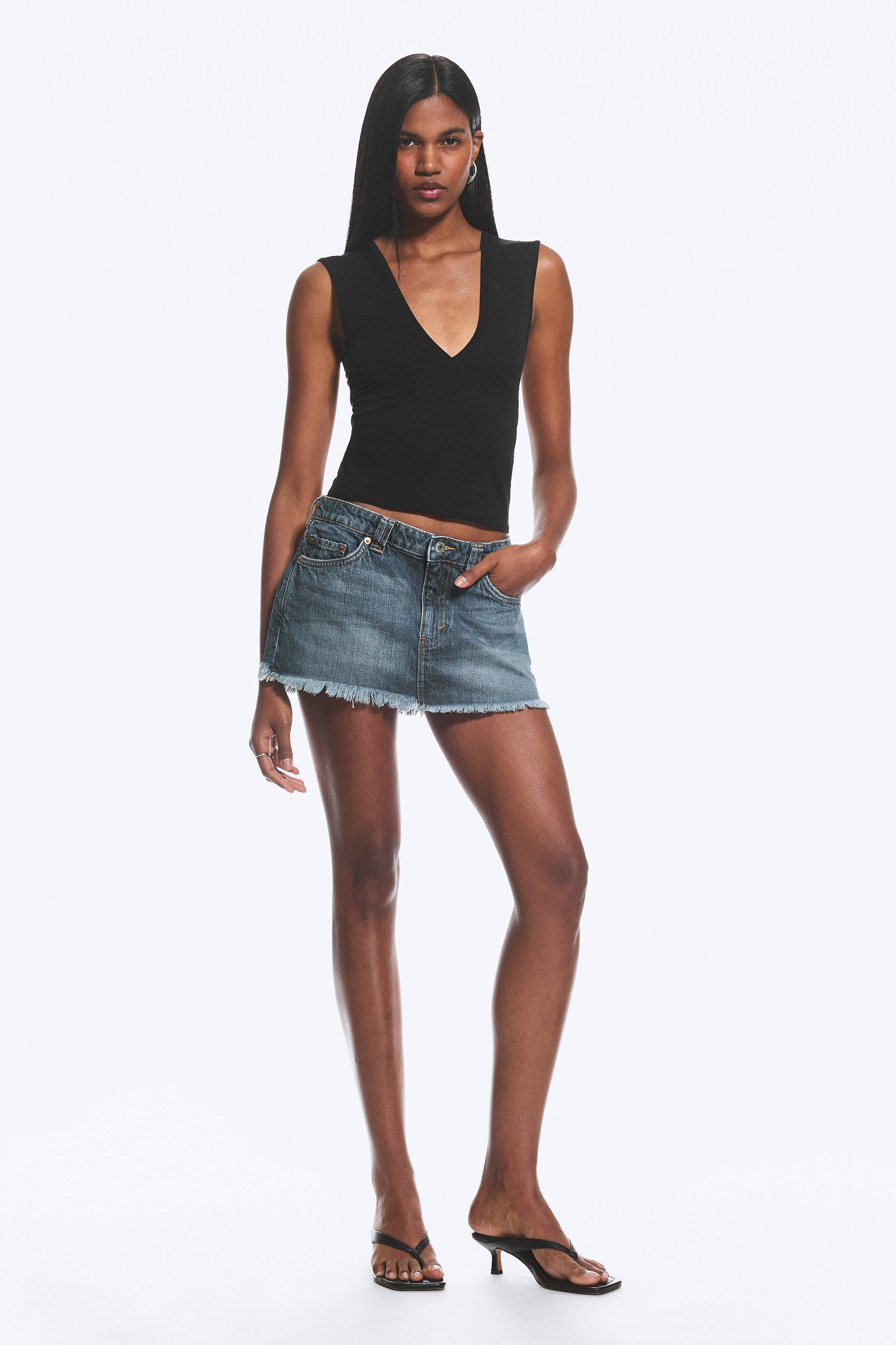 View larger image: Denim mini skirt in a medium blue wash with a frayed hem is worn by the model. The model places one hand in a front pocket of the skirt.