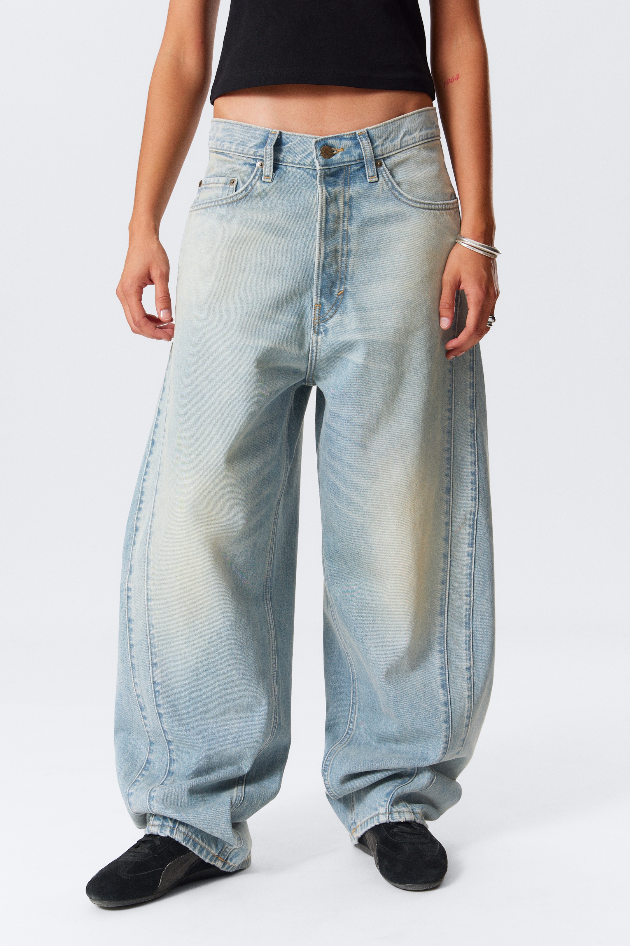 Visa större bild: Ljus tvätt, extremt baggy denimjeans visas upp, med en framträdande bredbenssilhuett som samlas vid anklarna. De är designade med distinkta vertikala formningssömmar som löper längs framsidan och baksidan av varje ben, vilket förstärker deras voluminösa struktur.