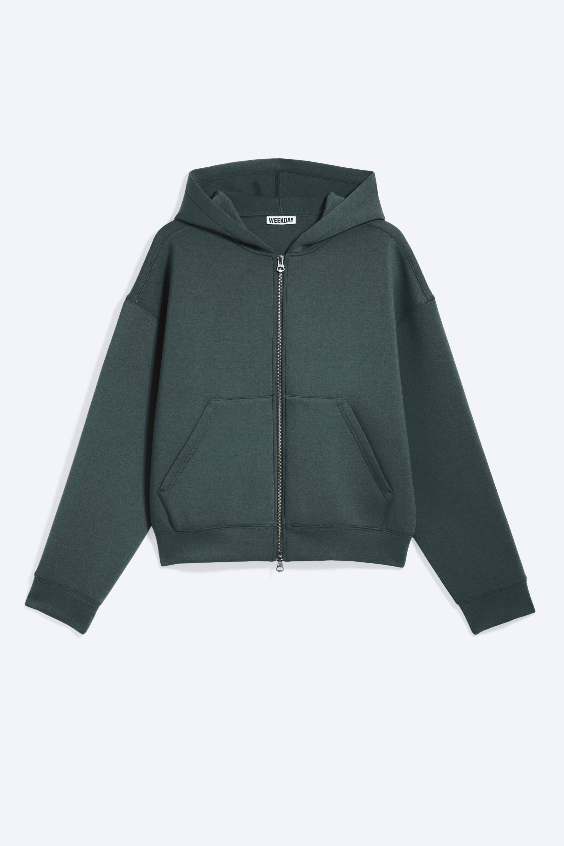 Visa större bild: En mörkgrön zip-up hoodie visas i en framifrån vy, utlagd platt. Den har en fullängds silverfärgad dragkedja, två rymliga framfickor och en fastsydd huva med en synlig "WEEKDAY"-märkesetikett.