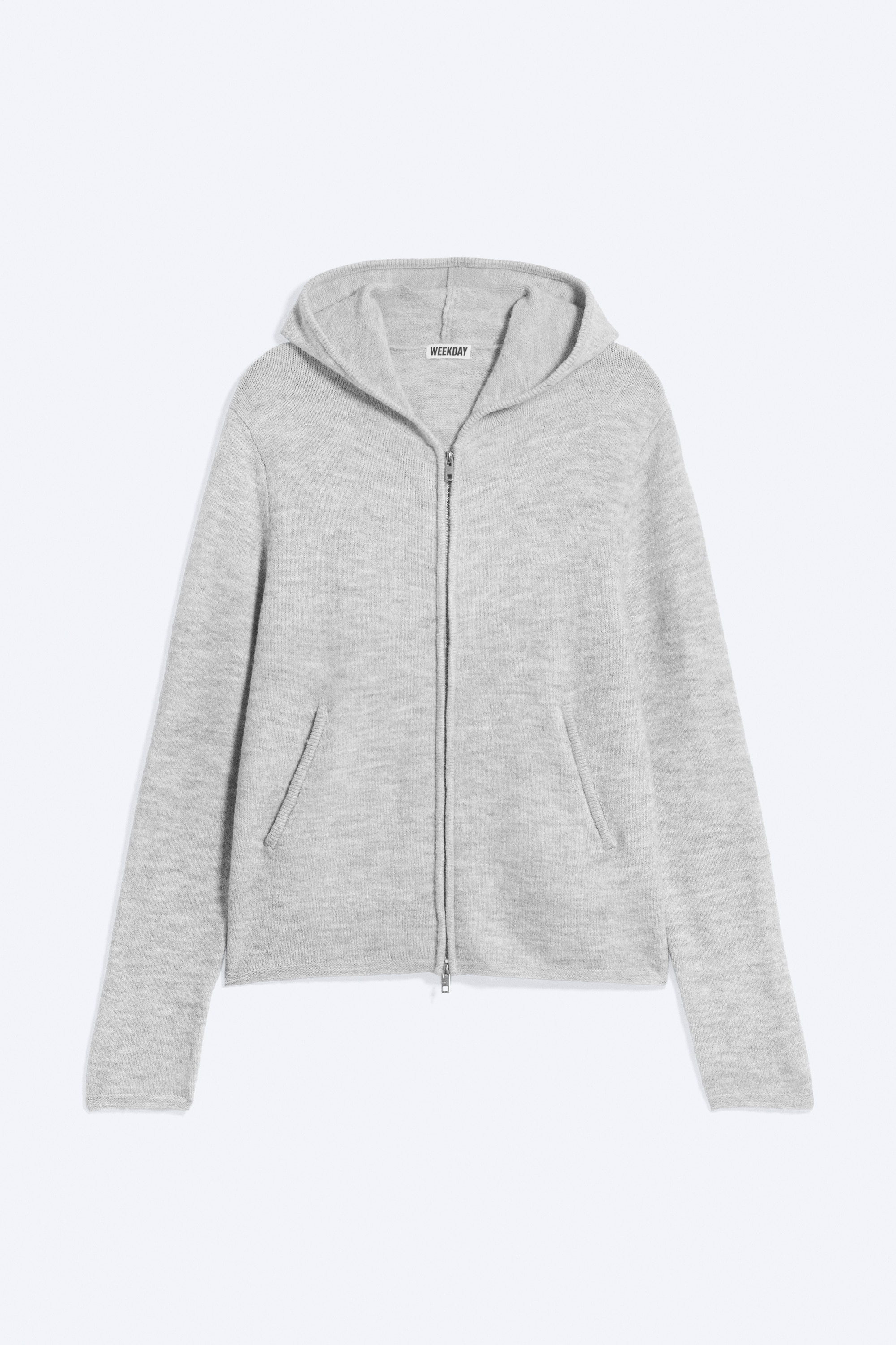 SvÄtle Å¡edÃ¡ pletenÃ¡ mikina s kapucÃ­ na zip je obleÄenÃ¡ na modelu, pÅiÄemÅ¾ kapuce je nataÅ¾enÃ¡ pÅes hlavu a paÅ¾e jsou zkÅÃ­Å¾enÃ© na hrudi. Mikina v leÅ¾Ã©rnÃ­m stÅihu mÃ¡ dvoucestnÃ½ kovovÃ½ zip, Å¾ebrovanÃ© lemy a Å¡ikmÃ© vÃ½pustkovÃ© kapsy, a je stylovanÃ¡ pÅes bÃ­lÃ© triÄko s dlouhÃ½m rukÃ¡vem a maskÃ¡ÄovÃ© kalhoty.
