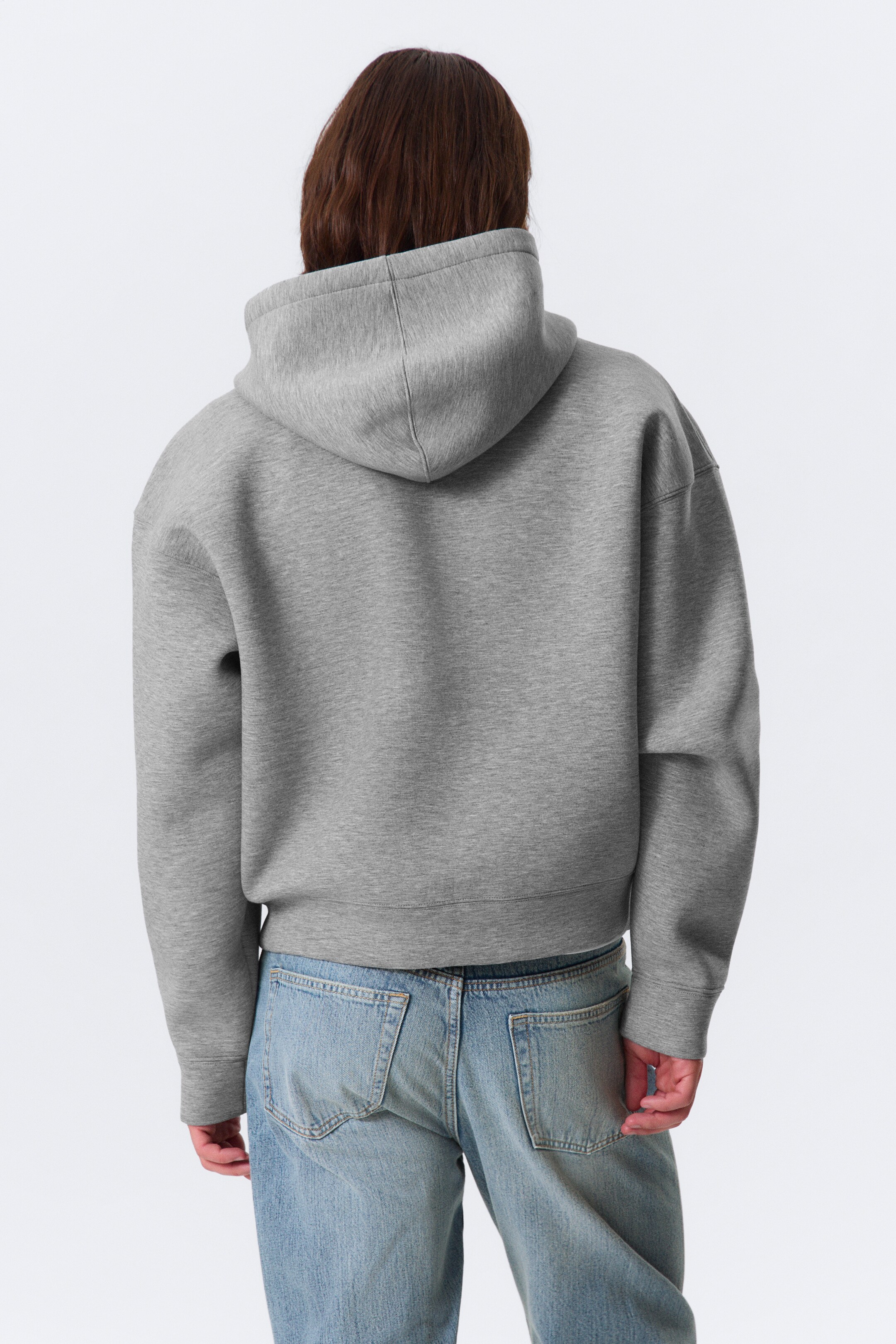 View larger image: A grey zip hoodie is being shown from the back, featuring a chunky scuba fabric, a regular fit with slightly dropped shoulders, ribbed cuffs, and a ribbed hemline.