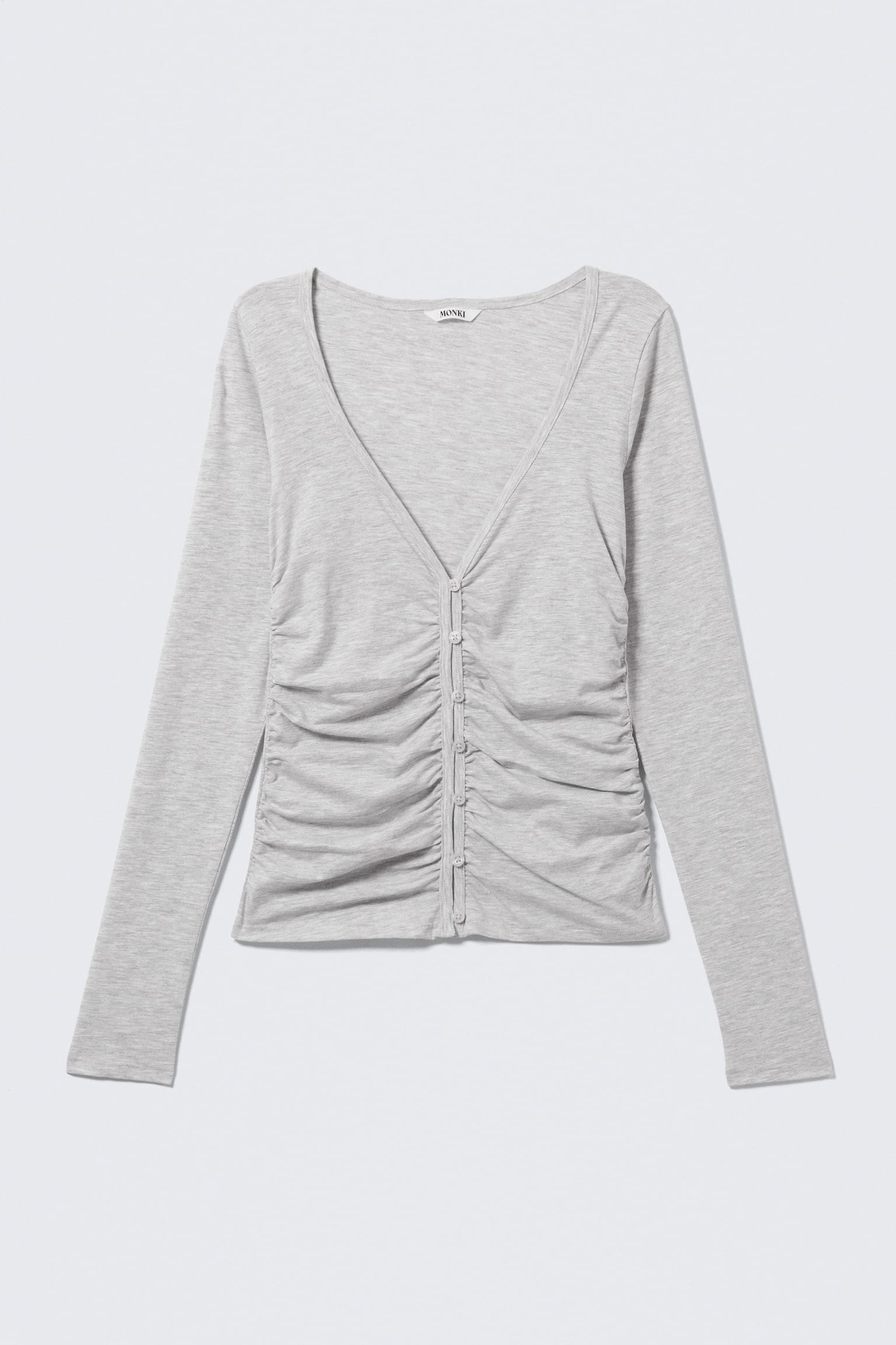 Un top de manga larga de color gris claro hecho de tejido de punto jaspeado se muestra desde el frente. Presenta un escote en V, una tapeta de botones en el centro delantera con botones pequeños y redondos, y fruncidos verticales que recogen la tela a ambos lados de la tapeta. - 1