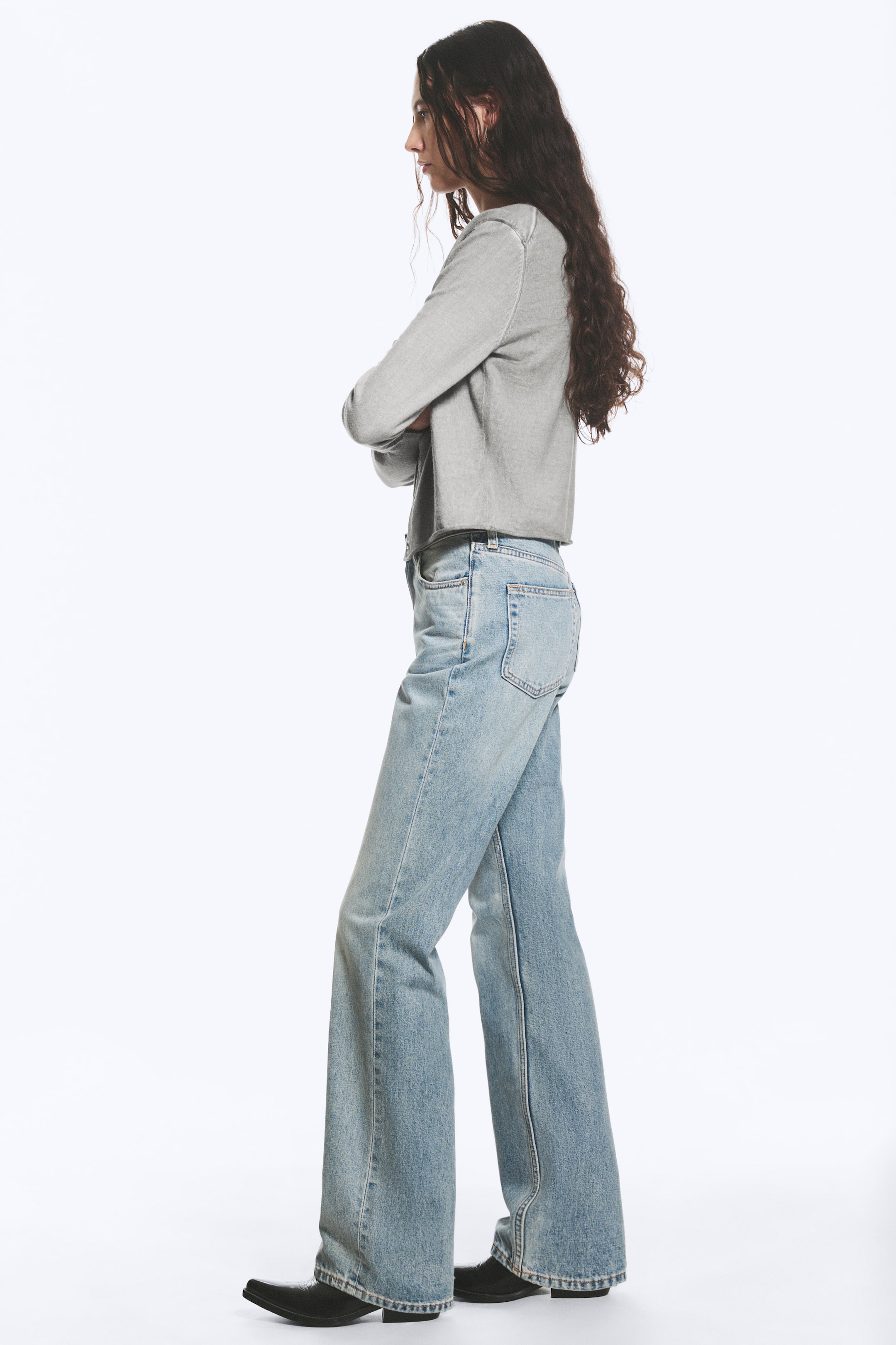 Agrandir l'image: Jeans évasés bleu clair présentés sous un angle latéral-arrière, arborant un délavage usé et une coupe décontractée qui s'évase à partir du genou, s'étendant sur des chaussures à bout pointu noires.