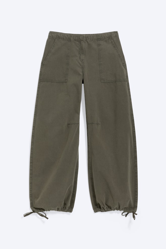 Diese olivgrünen Ballonhosen mit Kordelzug sind in einer frontalen Ansicht dargestellt und zeigen eine entspannte, weit geschnittene Silhouette, die an den Knöcheln mit gerafften, verstellbaren Kordelzügen zuläuft. Das Design verfügt über groÃe aufgesetzte Fronttaschen mit sichtbaren Steppnähten und dezente Knie-Nähte, die die voluminöse Form betonen. - 1