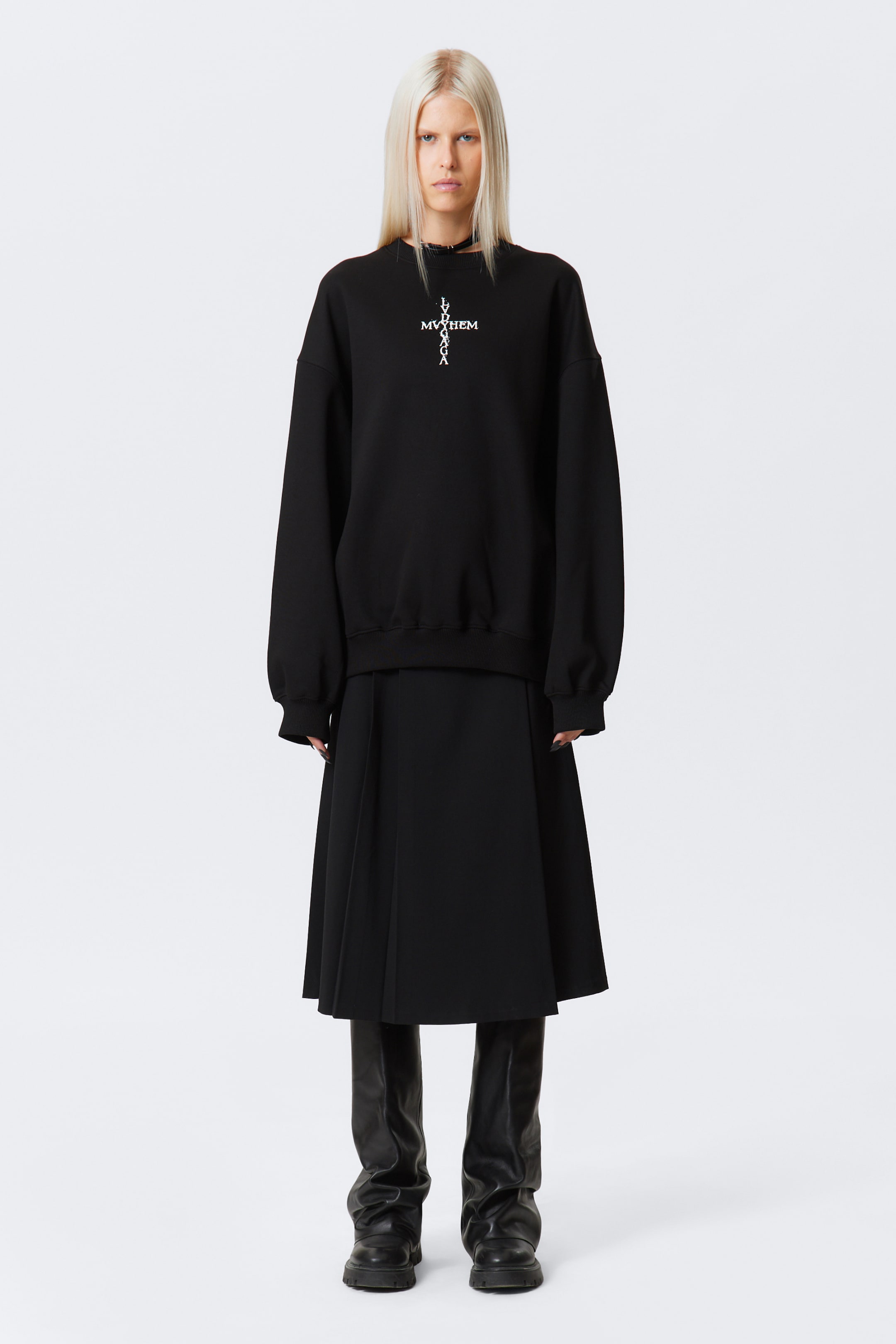 Agrandir l'image: Un sweat-shirt noir surdimensionné avec un col rond côtelé, des épaules tombantes, des poignets côtelés et un ourlet côtelé est porté par le mannequin, affichant un motif de croix graphique blanche sur le devant.