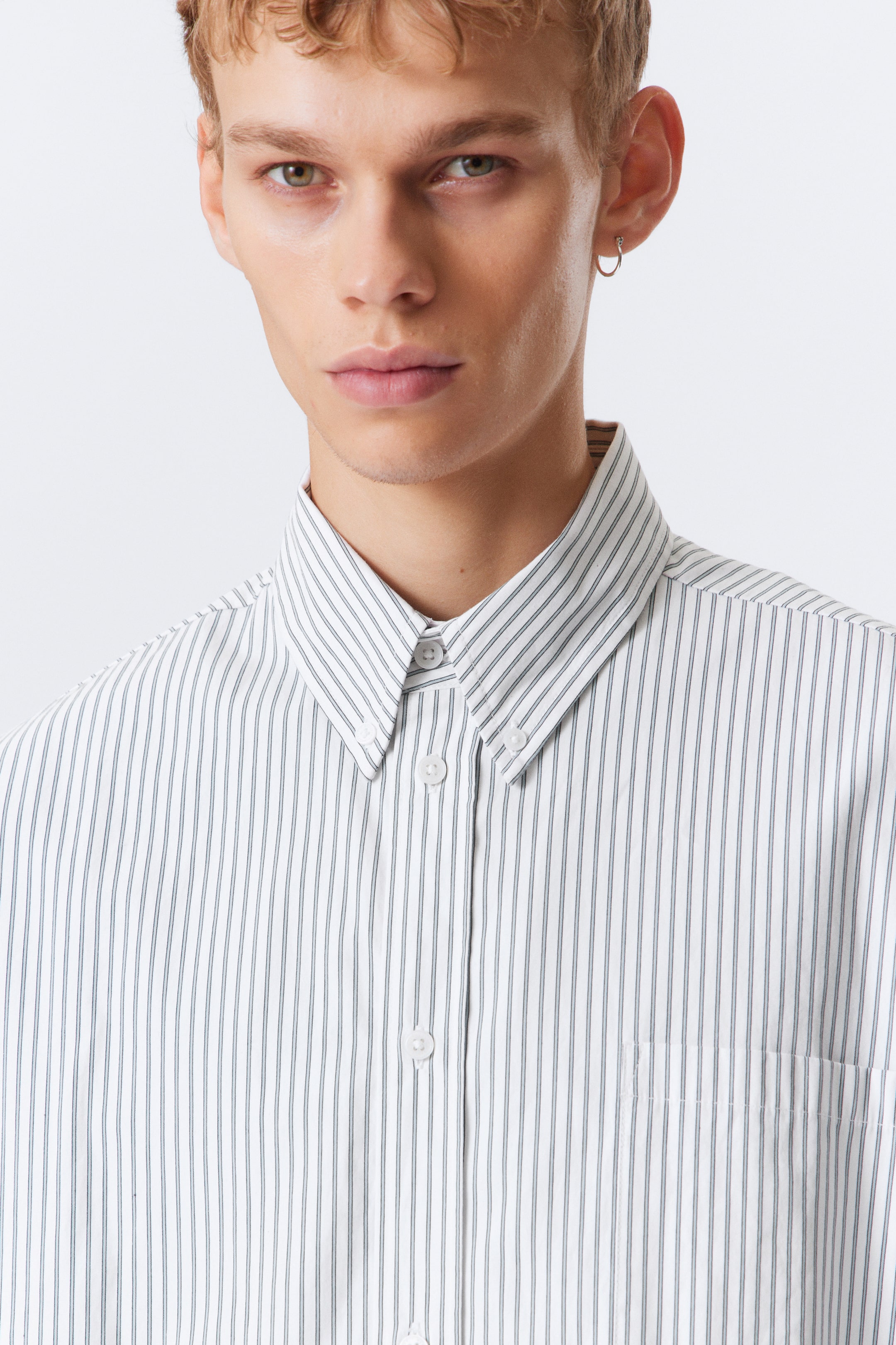 View larger image: A white button-down shirt is displaying thin vertical dark stripes, with its collar points secured by white buttons. White buttons are fastening the front placket, and a patch pocket is visible on the left chest.