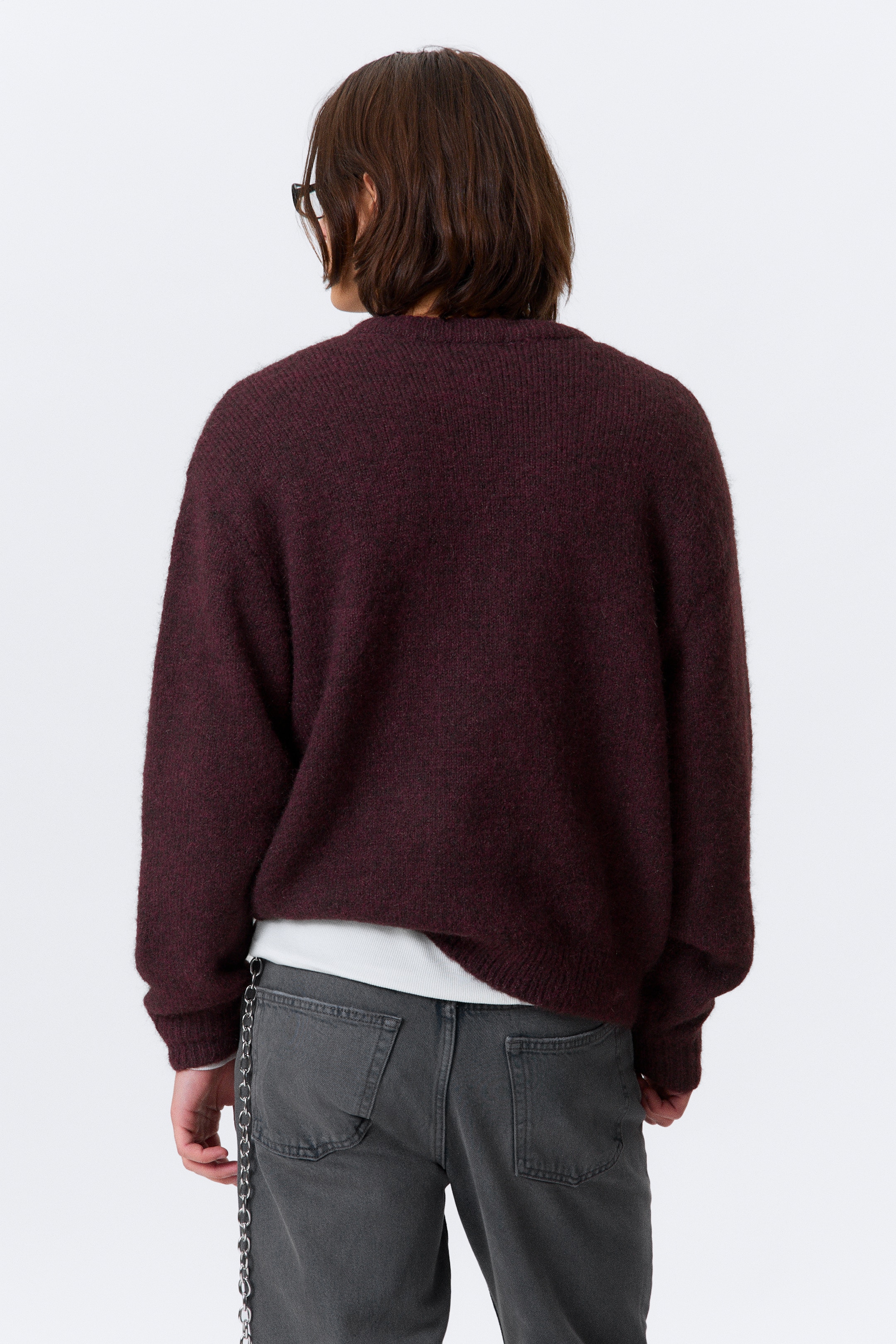 Visa större bild: En mörkröd tröja ses bakifrån, med en mjuk, luddig stickad textur och en överdimensionerad, avslappnad passform. En vit t-shirt är lagrad under, synlig vid fållen och manschetterna.