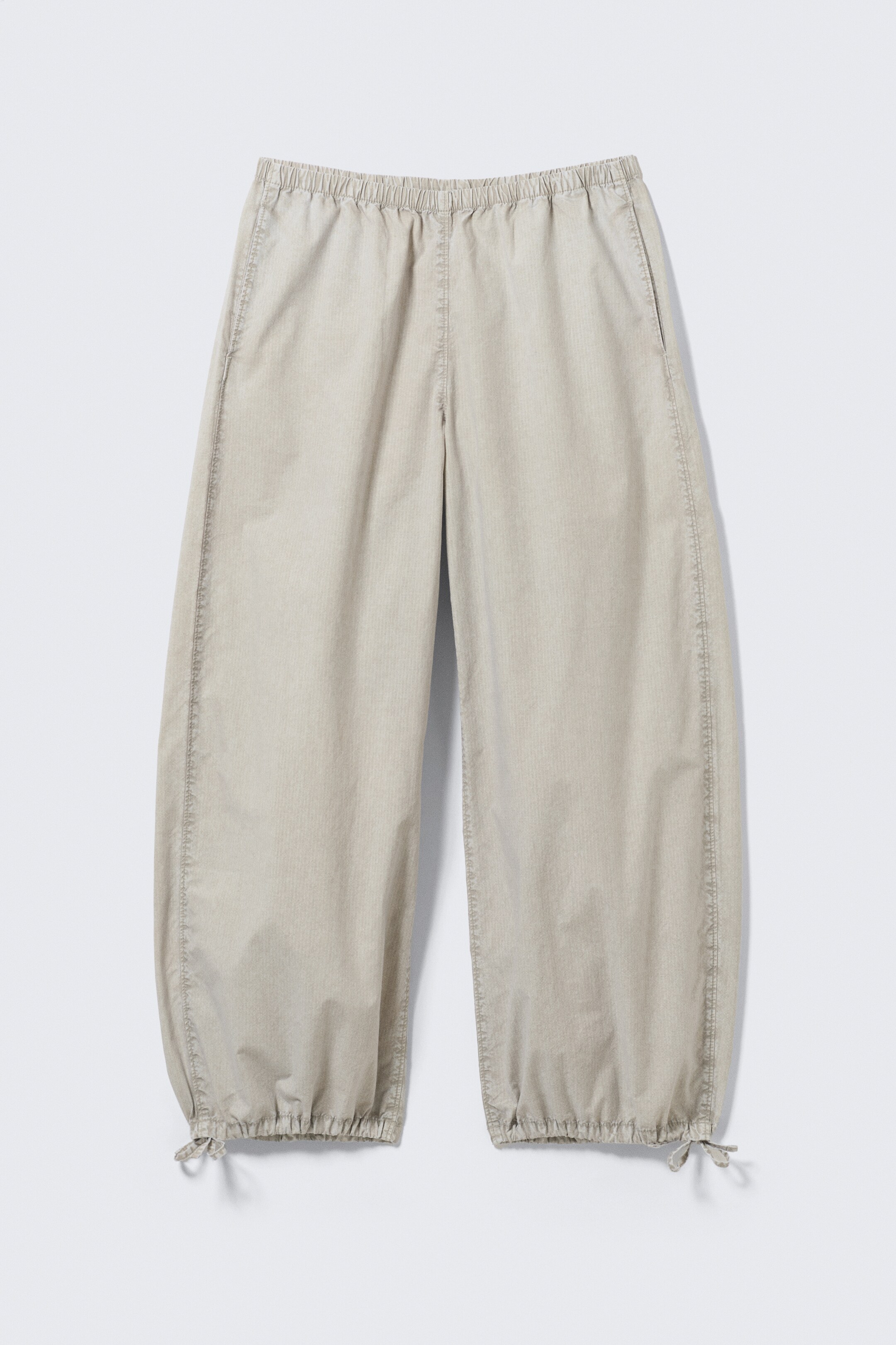 Visa större bild: Ljusbeige byxor visas i FRAMVY, med en elastisk, rynkad midja och sidofickor. De vida byxbenen smalnar av mot rynkade muddar, som är säkrade med knytband vid de yttre anklarna.