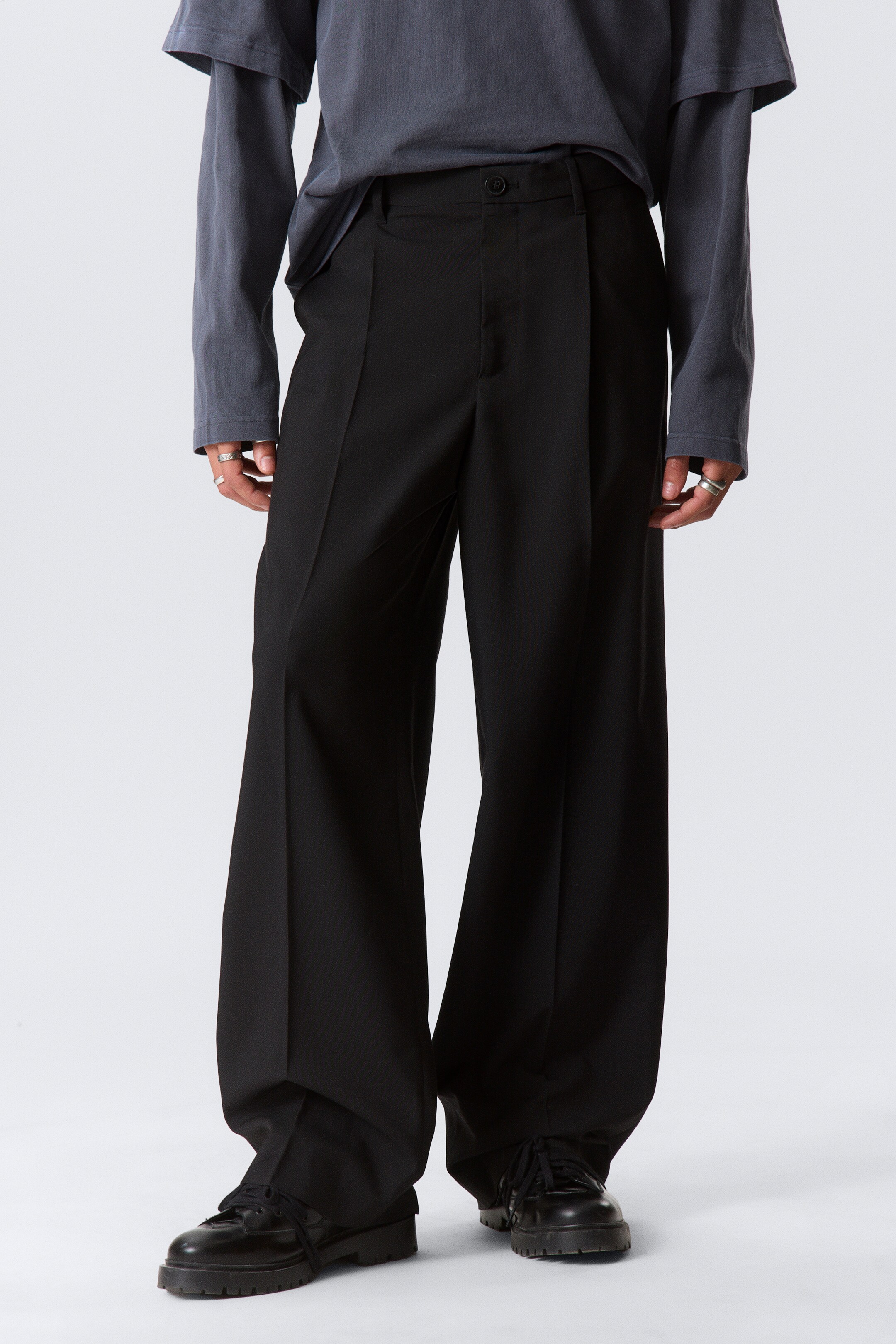 Agrandir l'image: Un pantalon large noir est porté, face à l'avant, avec de plis marqués à l'avant et une coupe pleine longueur qui s'étend sur des chaussures noires.