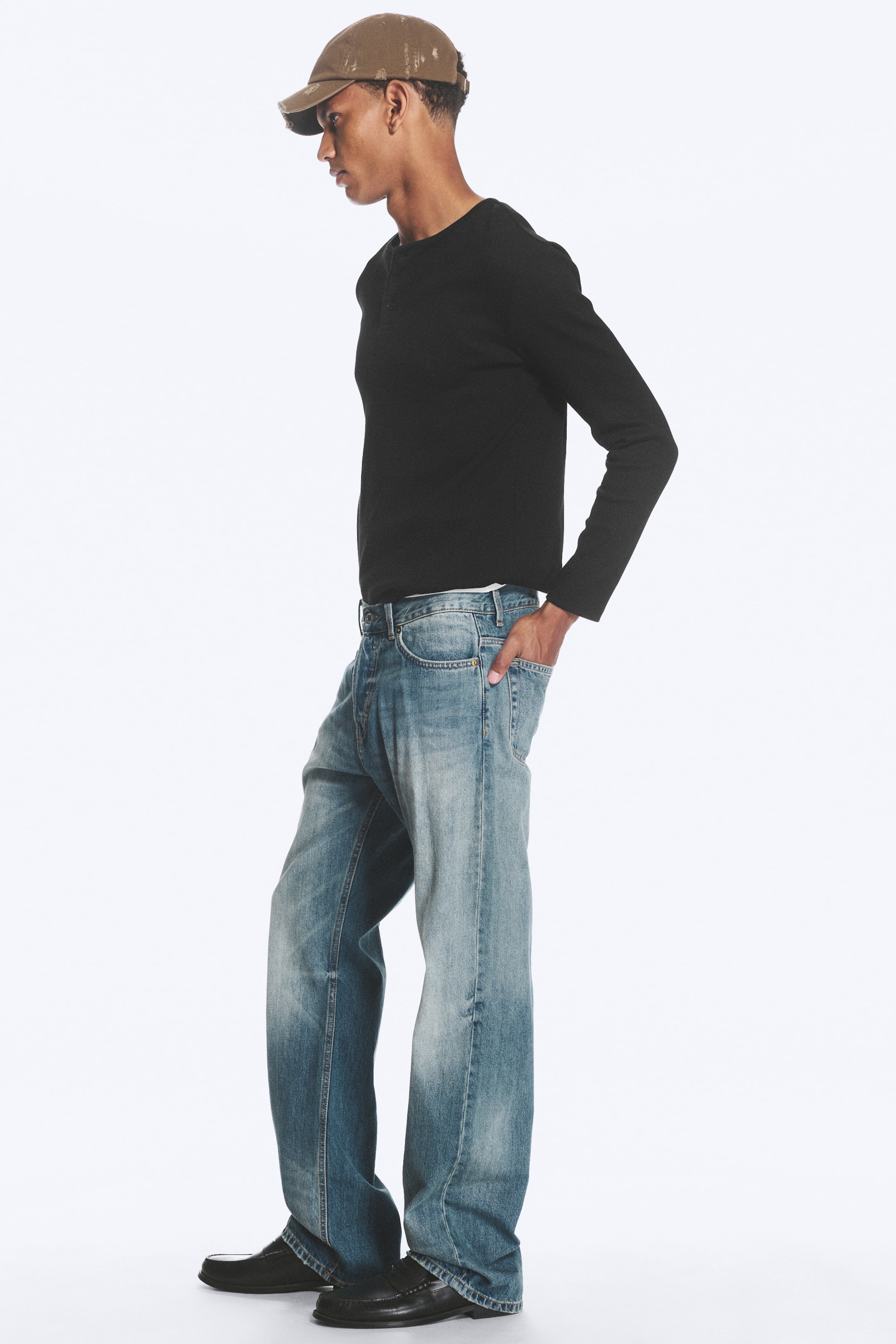 Grotere afbeelding bekijken: Mid-rise, relaxed-fit, straight-leg jeans in een lichtblauwe wassing, met een vijfzakkenontwerp en vervaging op de dijen en knieën, worden gedragen door het model. Het model plaatst één hand in een voorzak van de jeans.