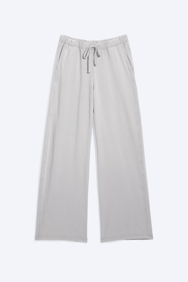 Light grey wide-leg trousers are presented in a front-facing view. They feature an elasticated waistband with a drawstring tied in a bow, and two side pockets. - 1