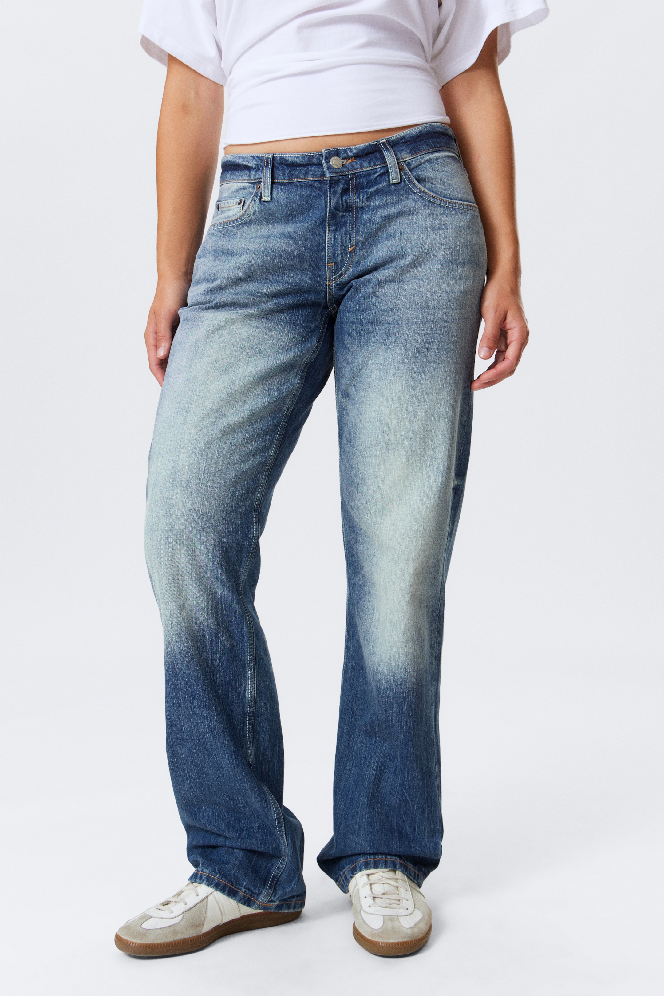 Visualizza immagine più grande: I jeans in denim blu presentano una vestibilità rilassata e a gamba dritta con un lavaggio scolorito, mostrando aree visibilmente più chiare sulle cosce e sulle ginocchia. La loro lunghezza completa si appoggia sulle scarpe di chi li indossa, creando un leggero accumulo all'orlo.