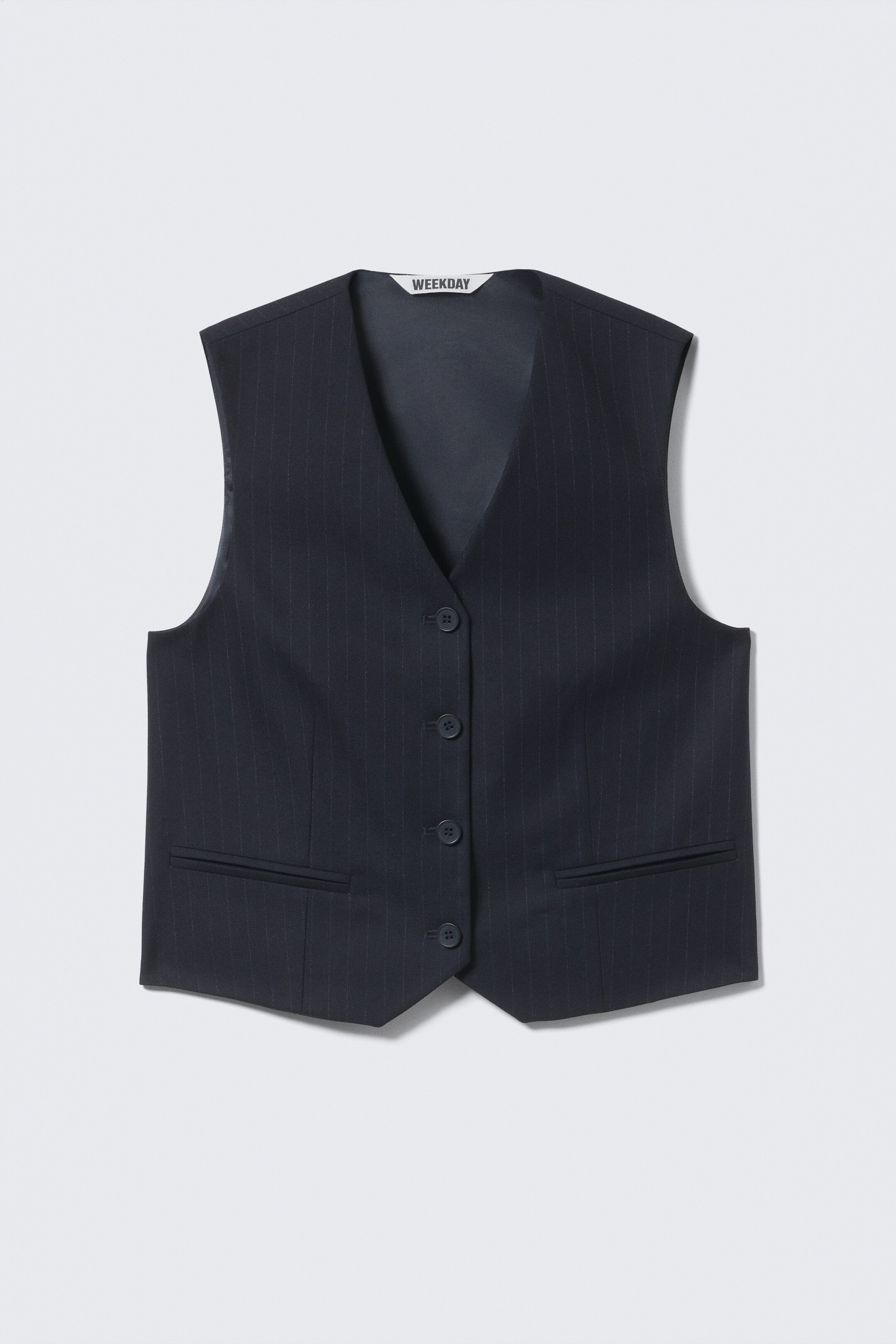 Agrandir l'image: Un gilet bleu foncé à simple boutonnage comporte de subtiles rayures verticales sur le devant. Il est conçu avec un col en V, une fermeture à quatre boutons et deux poches passepoilées.