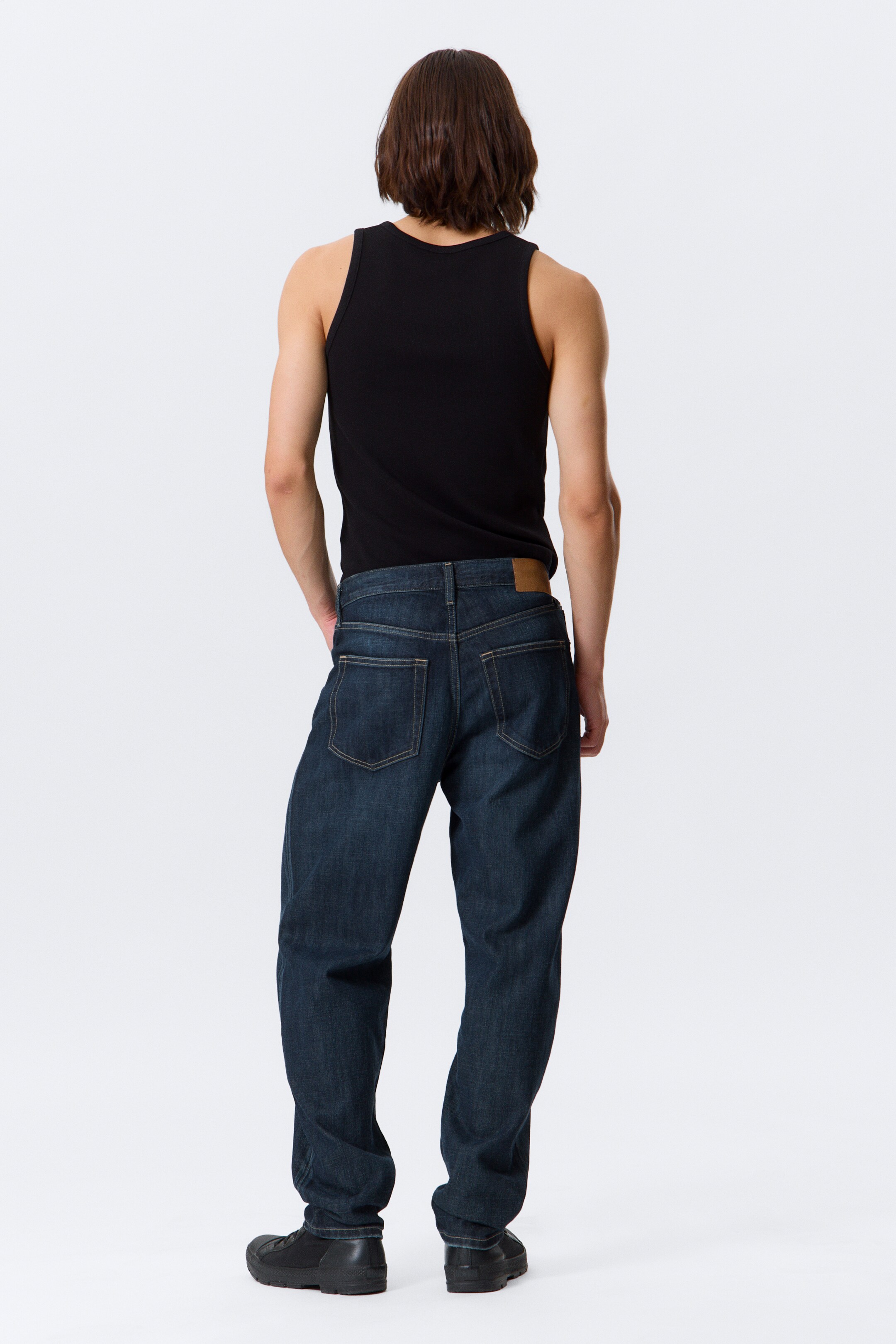View larger image: A pair of dark blue, relaxed fit jeans with a tapered leg is being presented from the BACK. They are featuring a rigid denim texture, a classic five-pocket design, and a tan brand patch on the back waistband.