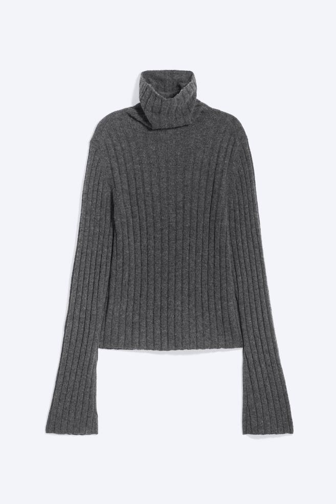A grey ribbed-knit turtleneck jumper is facing front, featuring a thick, folded turtleneck collar and long sleeves extending past the straight hem. The garment displays a consistent vertical rib-knit texture throughout. - 1