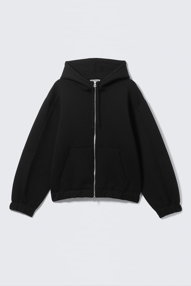 A black full-zip hoodie is shown from the front, featuring a silver-toned zip, an attached hood, and a large divided kangaroo pocket. It is designed with long raglan sleeves, detailed with patches, and finished with ribbed cuffs and a ribbed hem. - 1