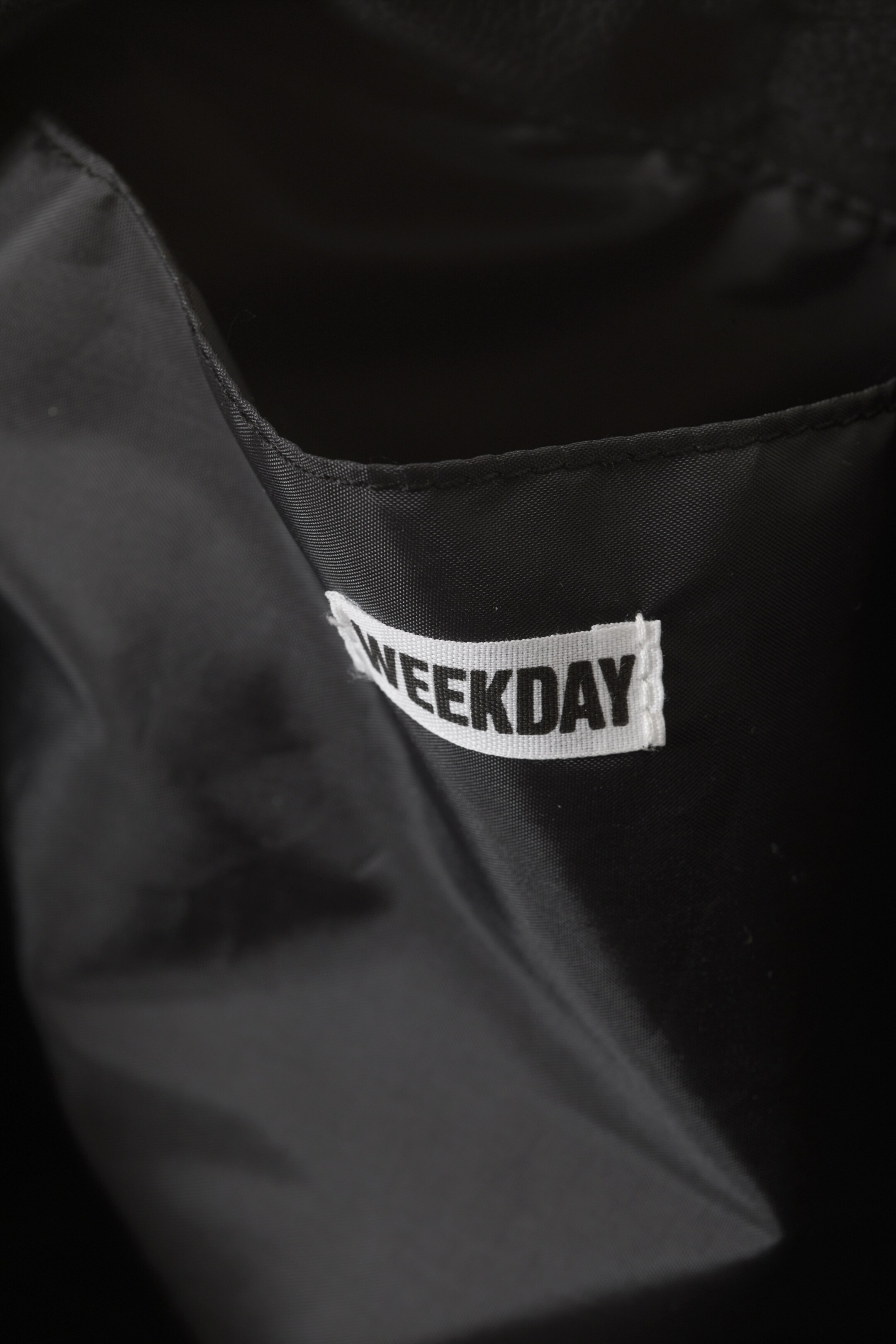 Agrandir l'image: L'intérieur d'un sac noir présente une étiquette de marque 'WEEKDAY' blanche attachée à une poche intérieure.