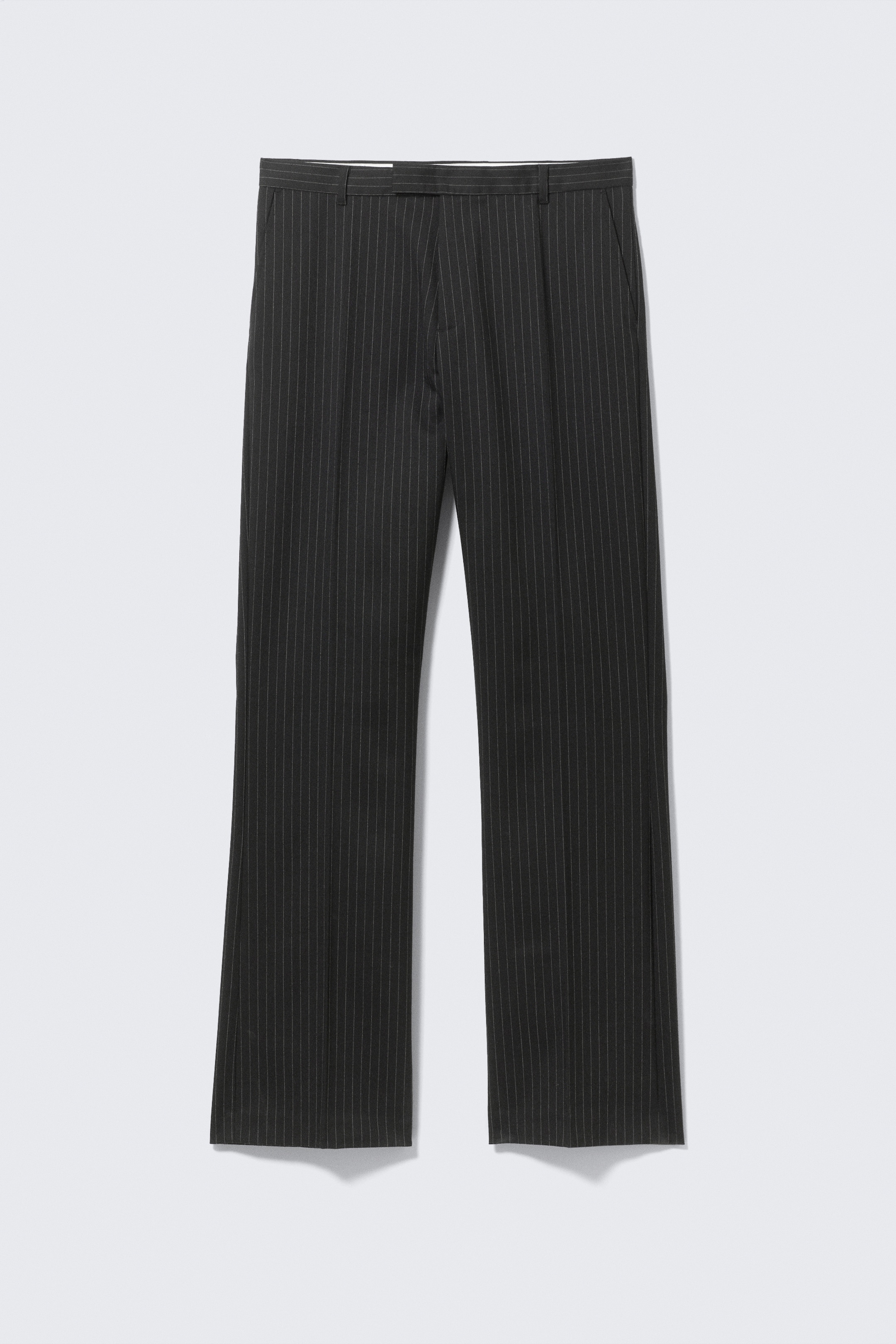 Agrandir l'image: Un pantalon à rayures fines gris foncé présente le DEVANT, avec de fines rayures verticales claires sur toute sa surface. Il est conçu avec une ceinture plate, des passants de ceinture, des poches latérales fendues et des jambes droites avec un pli subtil au centre qui descend le long du devant.