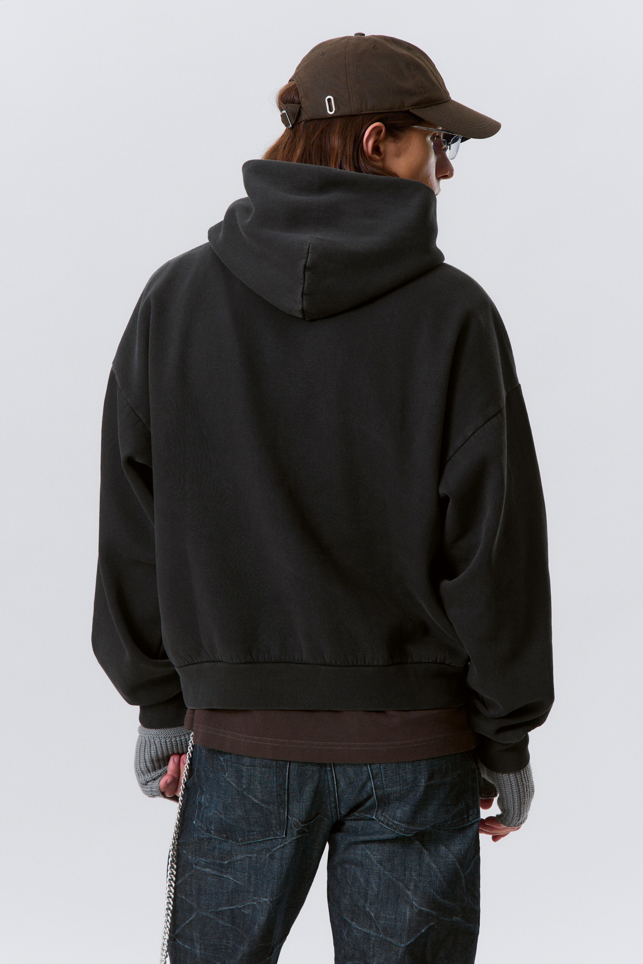 View larger image: A dark gray, relaxed-fit hoodie is being shown from the back. It is featuring a voluminous hood and a ribbed hem, and is layering over a brown t-shirt.