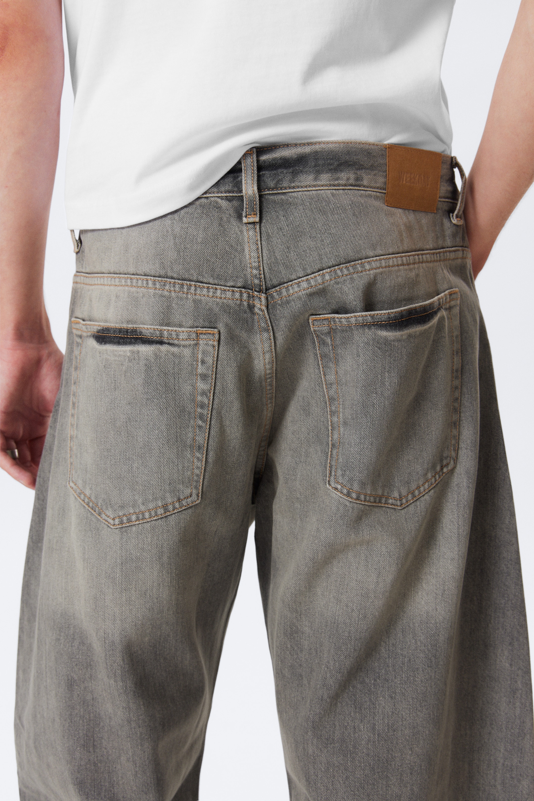 View larger image: Grey, wide-leg jeans are being shown from the back. The jeans are featuring a distressed wash with darker areas, two large back pockets with contrast stitching, and a brown patch on the right side of the waistband.