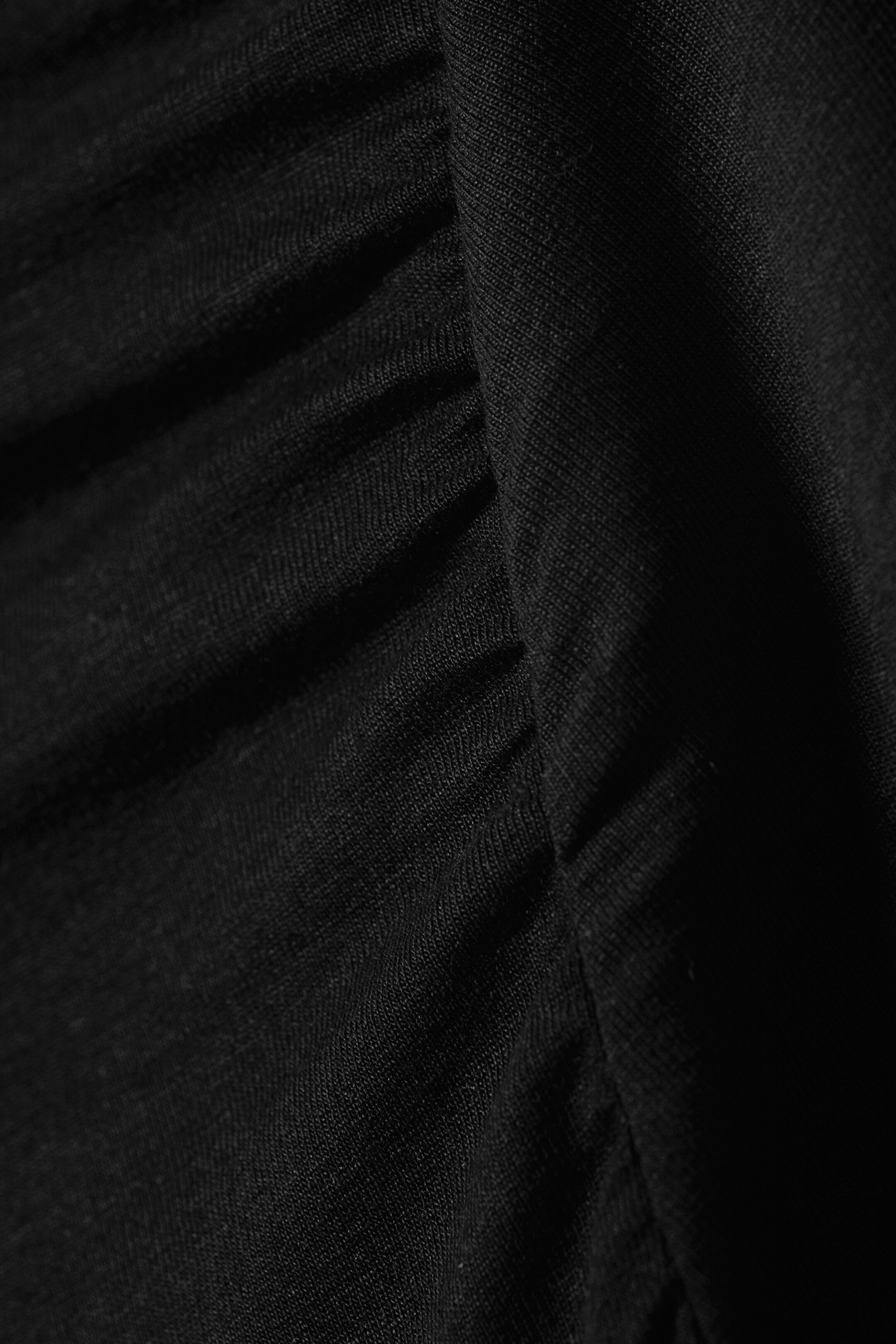 Vis større bilde: Et nærbilde av den svarte, stretchy lyocell jersey-kjolen viser vertikale rynker som skaper en teksturert, drapert effekt.