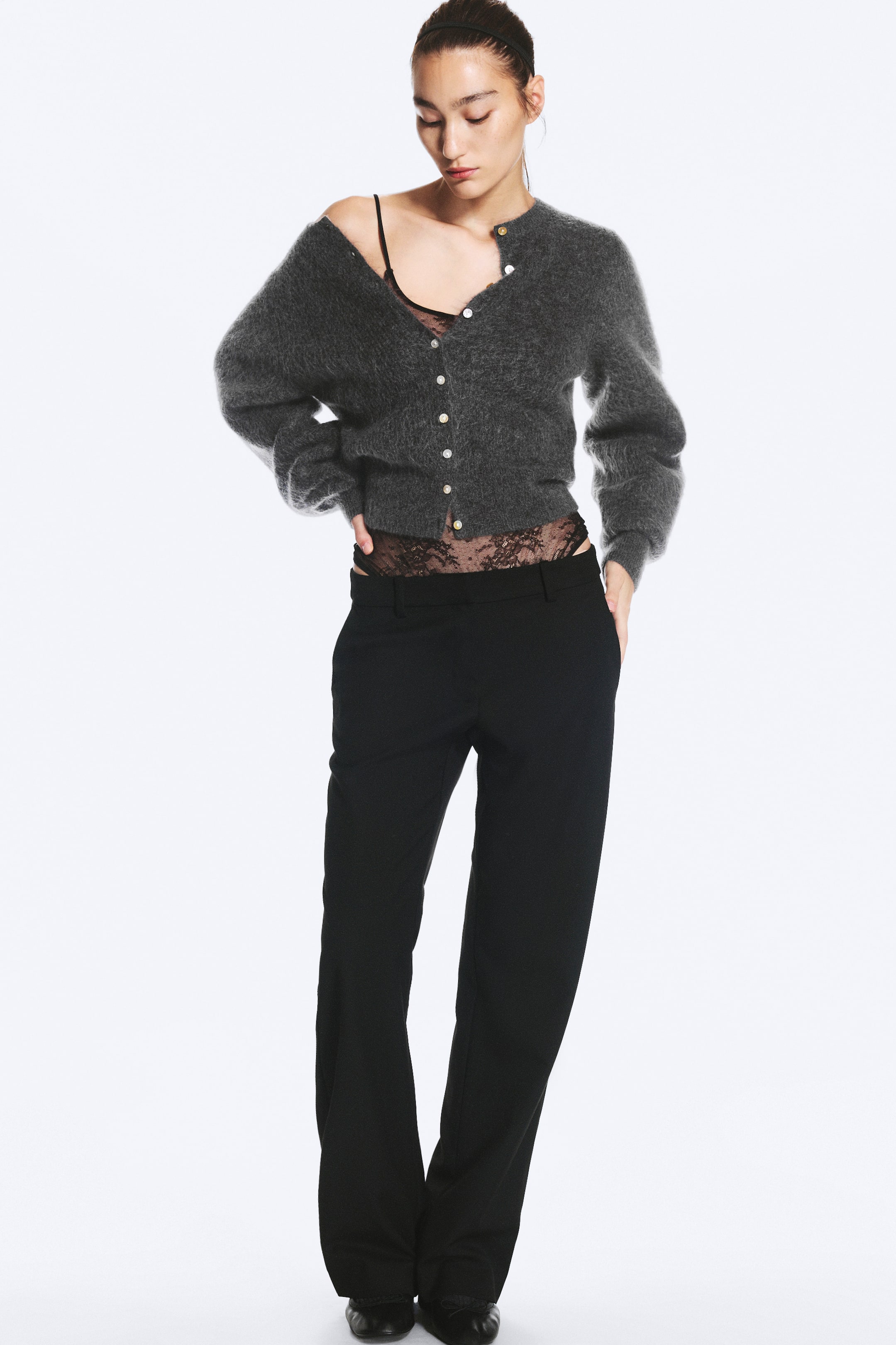 Visa större bild: Svarta kostymbyxor med låg midja, rak benvidd och bälteshällor bärs av modellen. Byxorna stylas med en grå stickad cardigan och en svart body i spets.