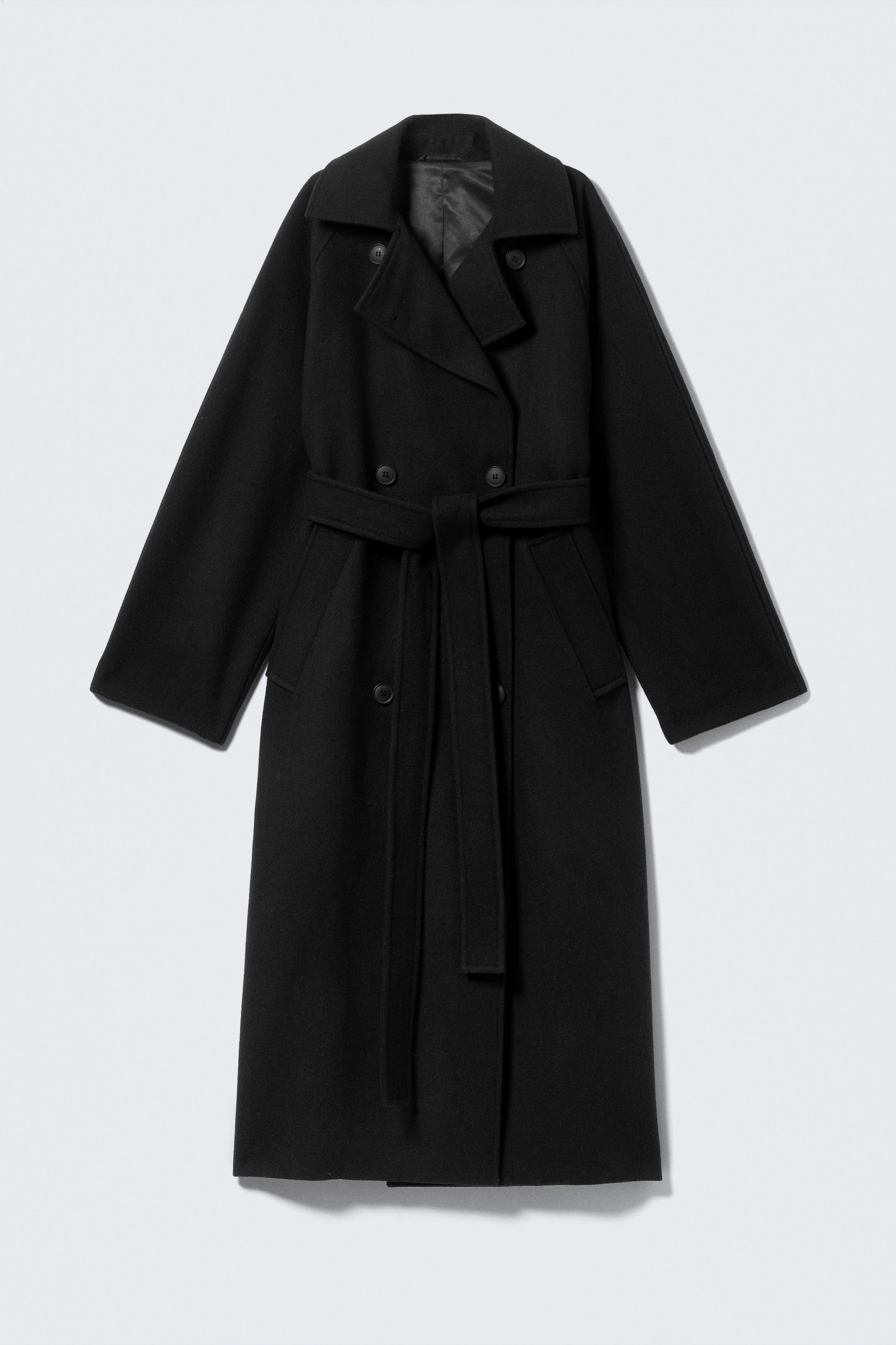 Visualizza immagine più grande: Un lungo cappotto nero oversize, presentato FRONT, presenta una finitura spazzolata e un davanti doppiopetto con ampi revers a lancia, maniche raglan e tasche a filetto. Una cintura staccabile è legata in vita e i bottoni tono su tono insieme alle cuciture a vista completano il suo design.