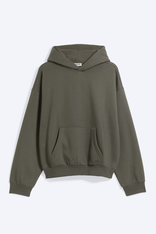 Una sudadera con capucha holgada de color verde oliva se muestra de frente, con un diseño de capucha plegada, hombros caÃdos y un amplio bolsillo canguro. La prenda de manga larga presenta puños acanalados y un bajo acanalado con un sutil fruncido que crea una silueta redondeada. - 1