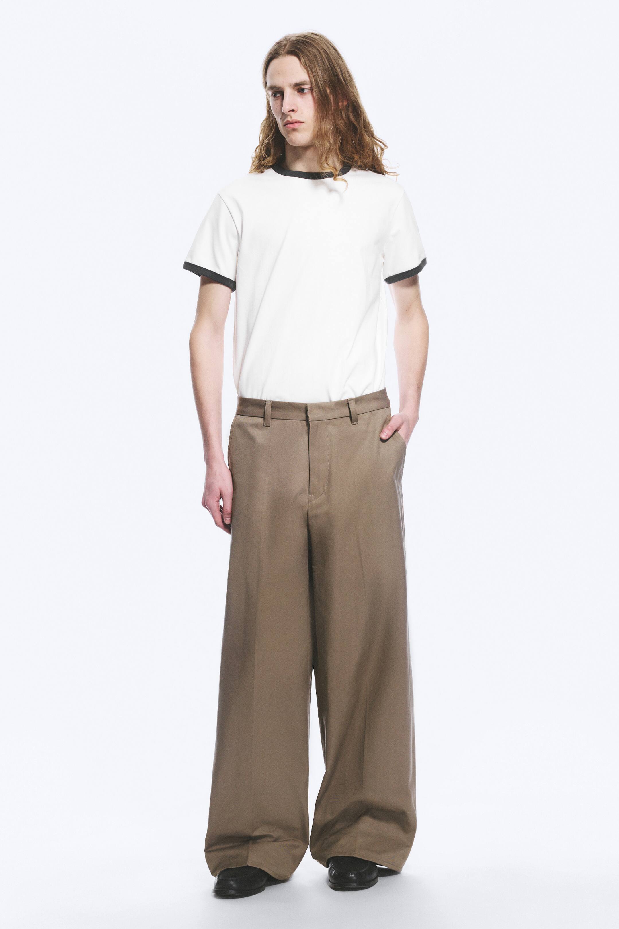 Zobacz większy obraz: Biała koszulka typu ringer jest prezentowana przodem. Charakteryzuje się czarnym, prążkowanym kołnierzykiem oraz czarnymi, prążkowanymi mankietami na krótkich rękawach, a także jest włożona w brązowe spodnie.