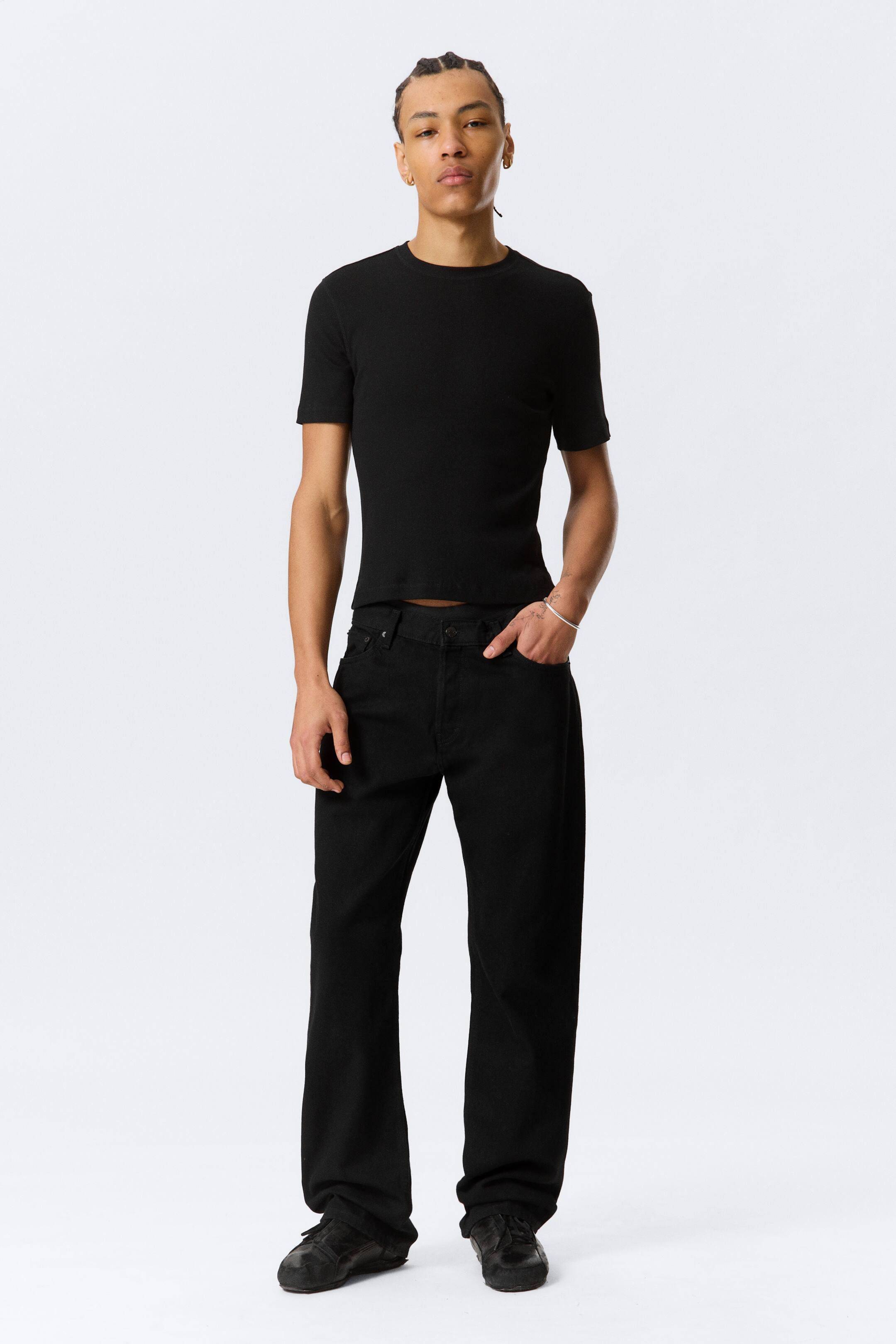 Visa större bild: En svart, åtsittande, kortärmad, ribbad tröja med rund hals bärs tillsammans med svarta, löst sittande, raka jeans, presenterad i en fullängdsbild framifrån.