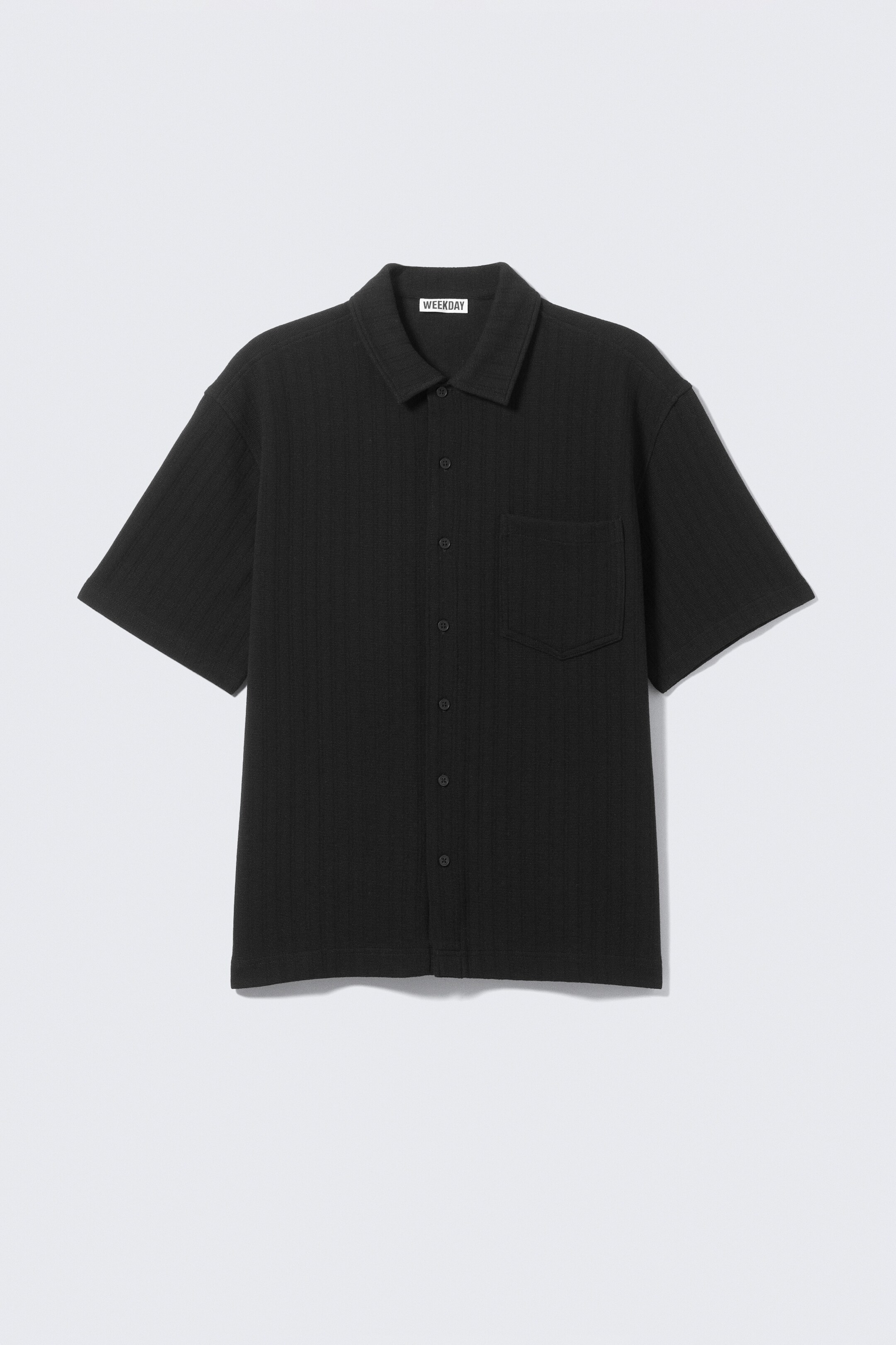 Vezi imaginea mai mare: Un tricou negru cu mâneci scurte își etalează partea din FAȚĂ, evidențiind o croială lejeră și o textură tricotată fin. Are un guler ascuțit, o închidere cu nasturi frontali vizibili negri și un buzunar unic la piept pe partea stângă, oferind un aspect curat și minimalist.