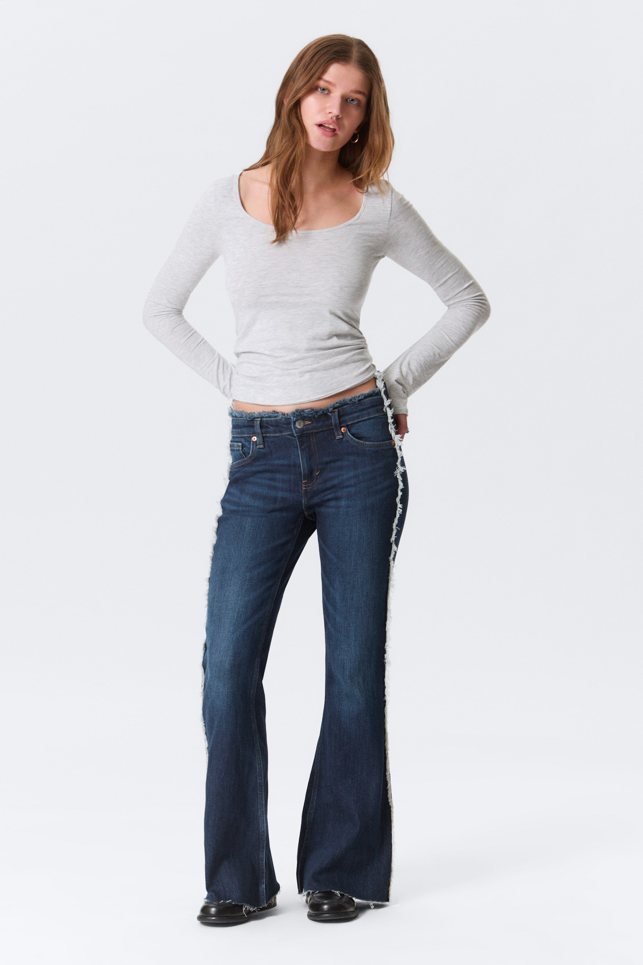 Se større billede: De mørkeblå, vidt udsvingende jeans har en rå, frynset linning, frynsede sidesømme og en rå kant, der præsenterer en frontudsigt.