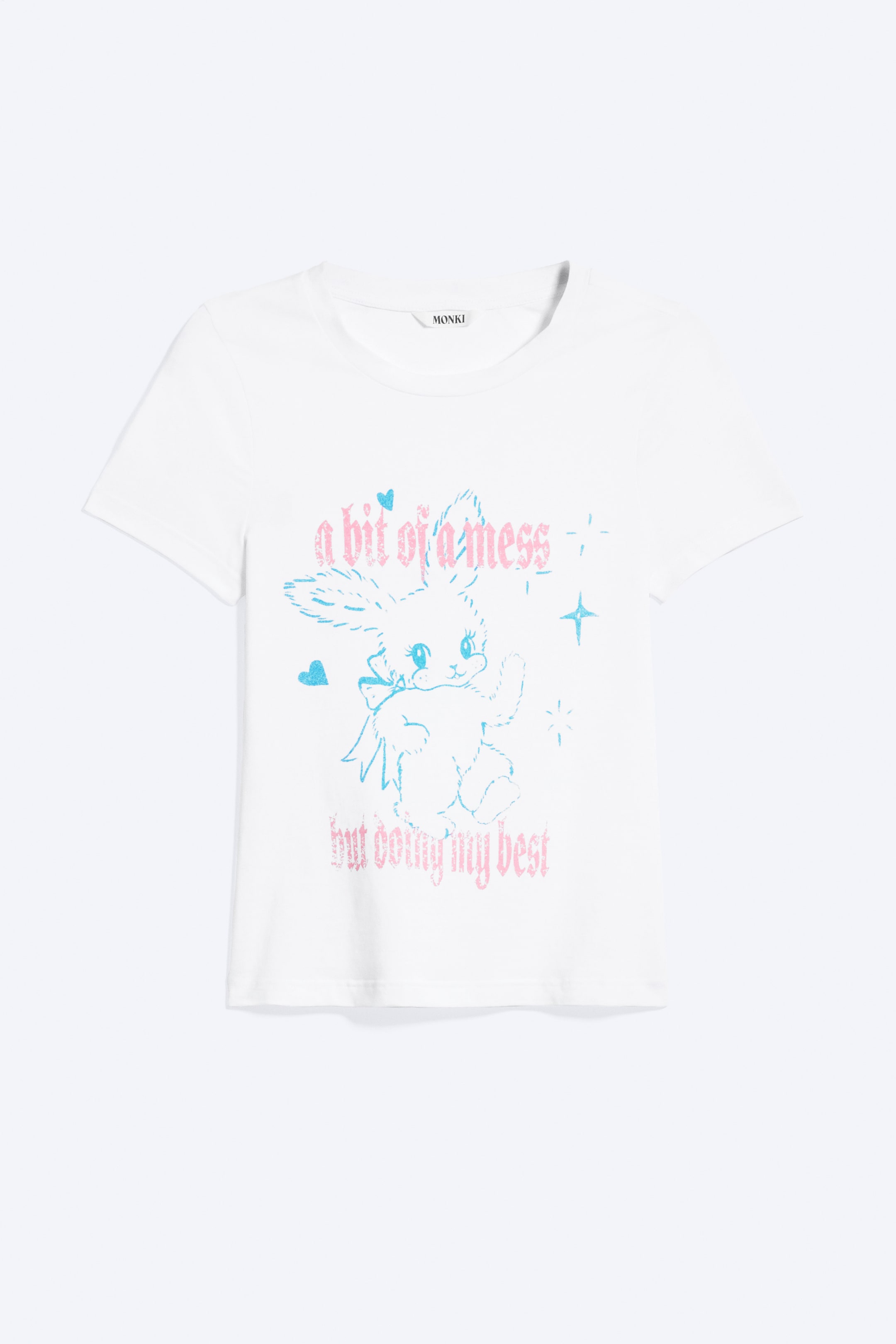 Größeres Bild anzeigen: Ein weißes T-Shirt ist frontal abgebildet, mit einem Rundhalsausschnitt und kurzen Ärmeln. Ein zentrales Grafikmotiv zeigt einen im Cartoon-Stil gehaltenen, leicht ramponierten Hasen mit Schleife, umgeben von Herzen und Sternen, in hellblauen und rosa Tönen, mit den Sätzen „a bit of a mess“ oben und „but doing my best“ unten.