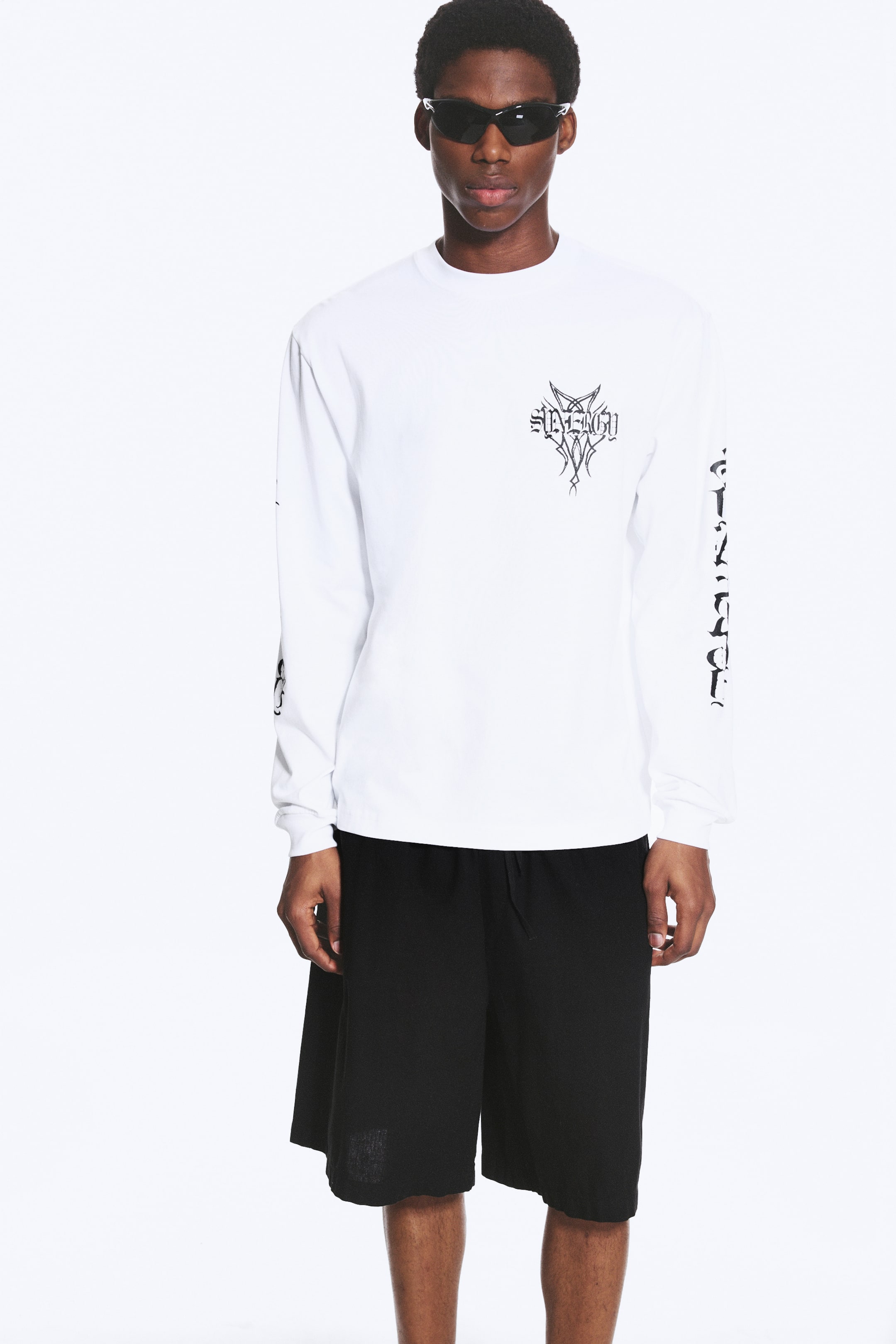 Visualizza l'immagine ingrandita: Una t-shirt bianca a maniche lunghe presenta un girocollo, una stampa grafica nera sul petto e ulteriori stampe grafiche nere che si estendono lungo entrambe le maniche.