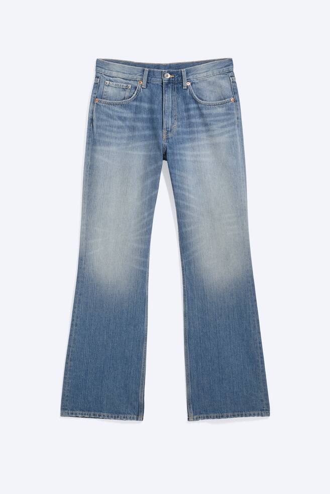 Ein Paar mittelhoch geschnittene, locker sitzende Bootcut-Jeans wird von vorne gezeigt und präsentiert ein mittelblaues, streifiges Denim mit helleren Verwaschungen an den Oberschenkeln und Knien. Die Jeans verfügt über zwei Fronttaschen, eine Münztasche und einen sichtbaren Reißverschluss mit Knopfverschluss. - 1