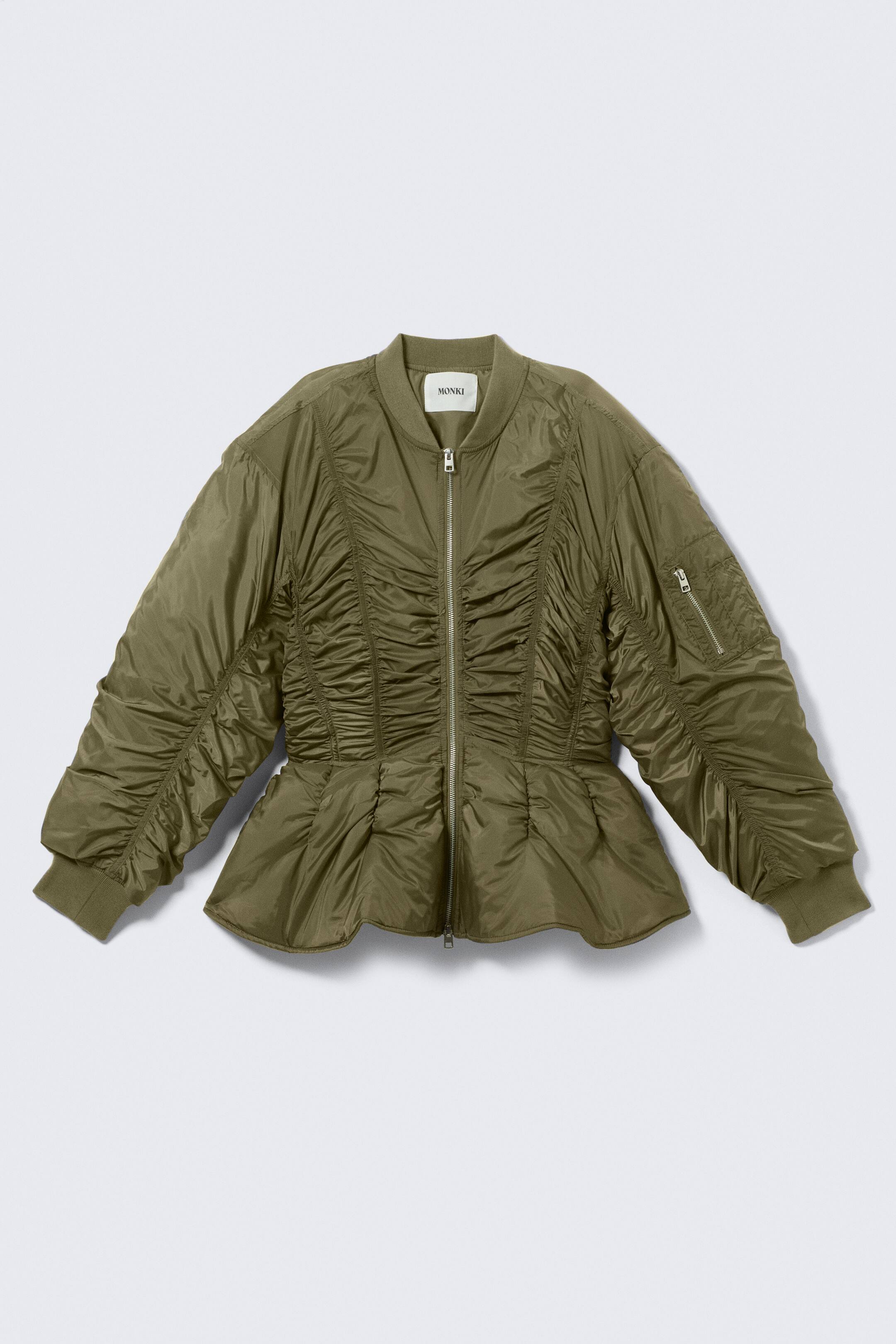Ver imagem maior: Um blusão bomber verde azeitona está a apresentar uma vista FRONTAL, com fecho de correr completo, gola alta canelada e punhos canelados. Um franzido vertical extenso detalha o corpete frontal e as mangas, criando uma bainha em estilo peplum, e um bolso utilitário com fecho é visível na manga esquerda.