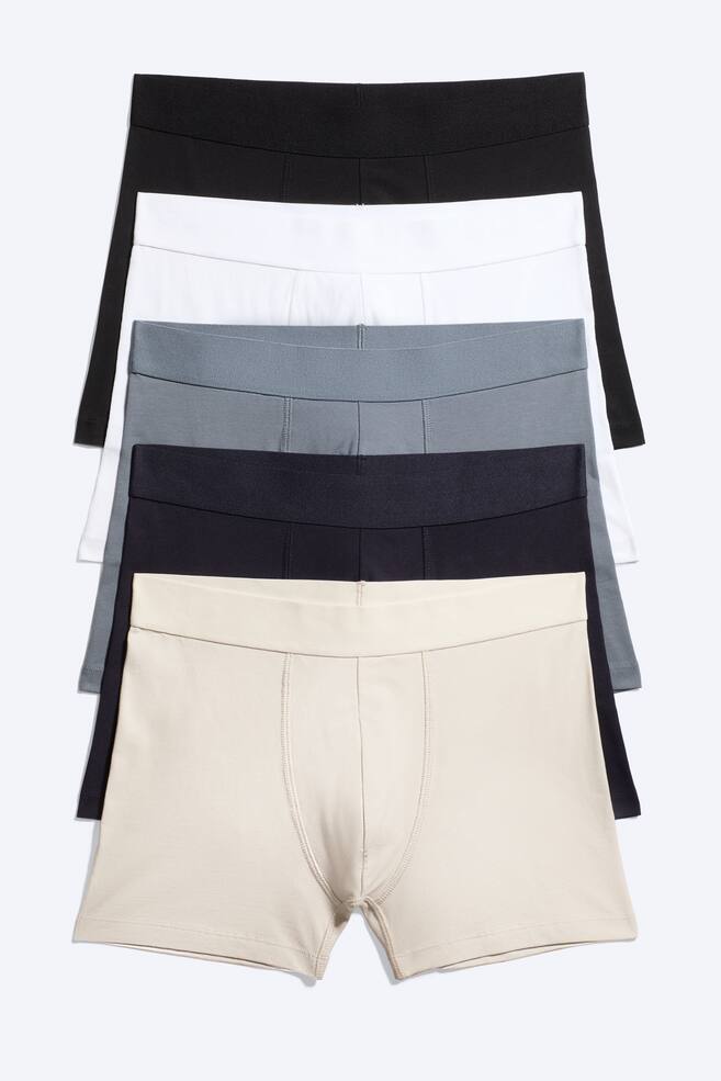 Five boxer briefs are arranged in a stack, presented from the front. They display a colour sequence from top to bottom: black, white, grey, navy, and beige. Each boxer brief features a wide elastic waistband, and the frontmost beige pair shows a contoured pouch with visible stitching. - 1